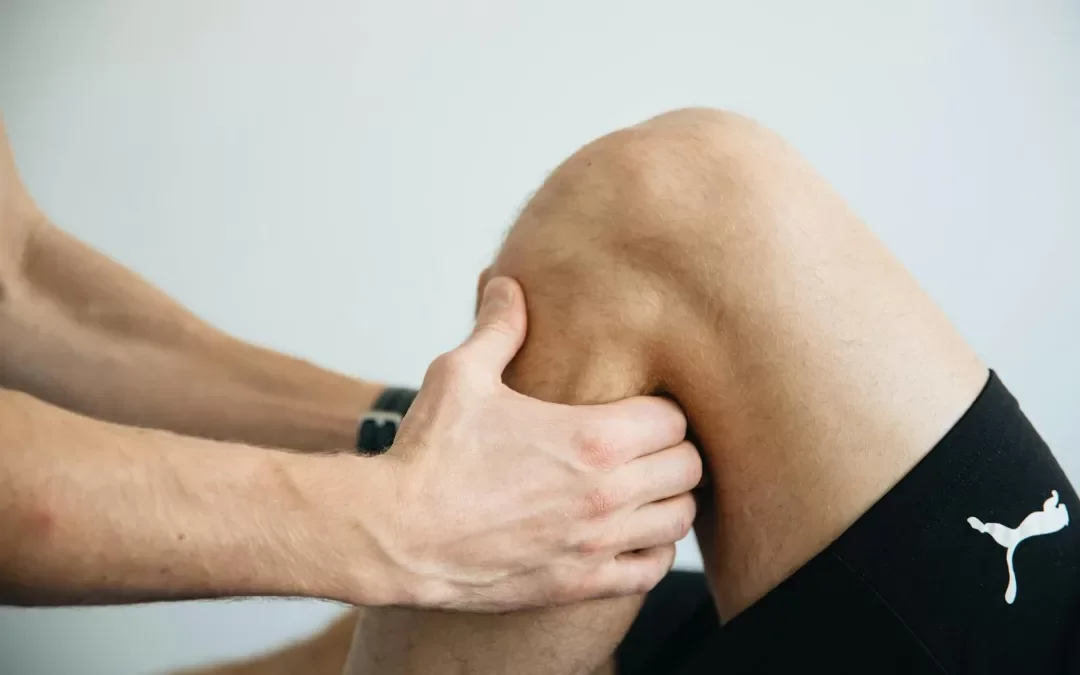 A person receiving a physical therapy or massage on their knee, with hands placed on the knee cap and surrounding area.