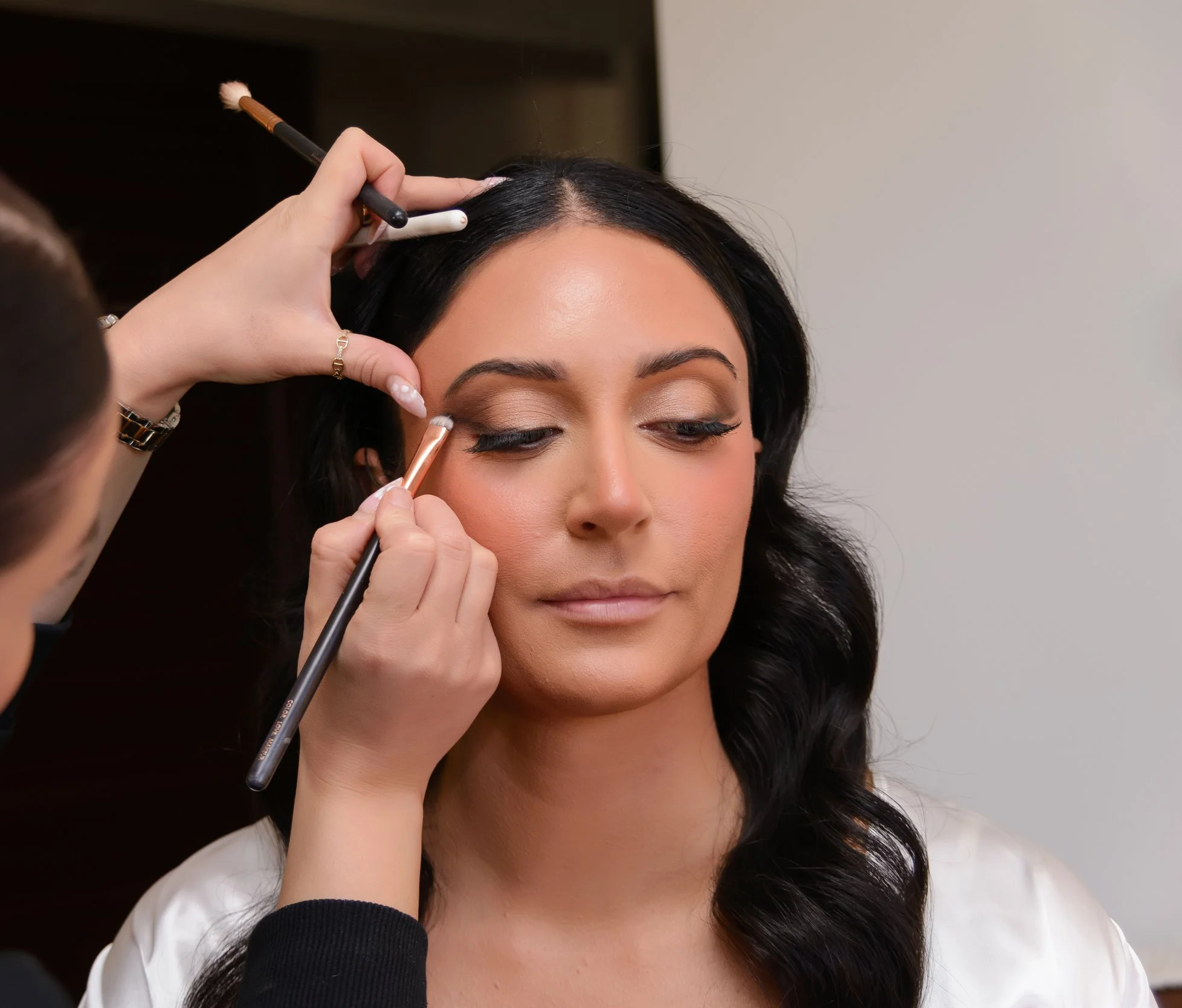 Makeup artist applying eyeshadow to a woman's eyelid with a brush.