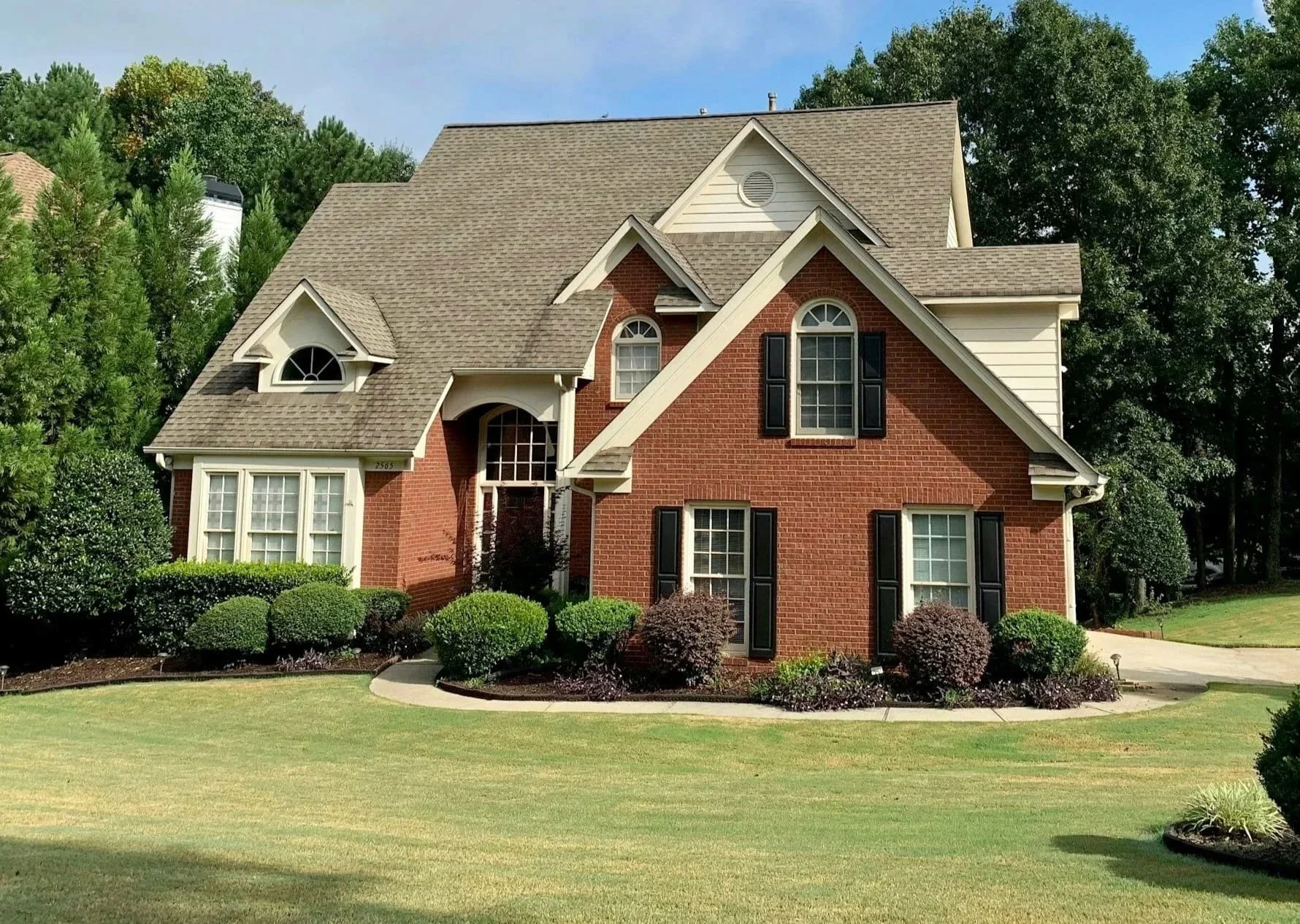 Photo of a large brickhome with with a well maintained yard, new landscaping and a wooded lot