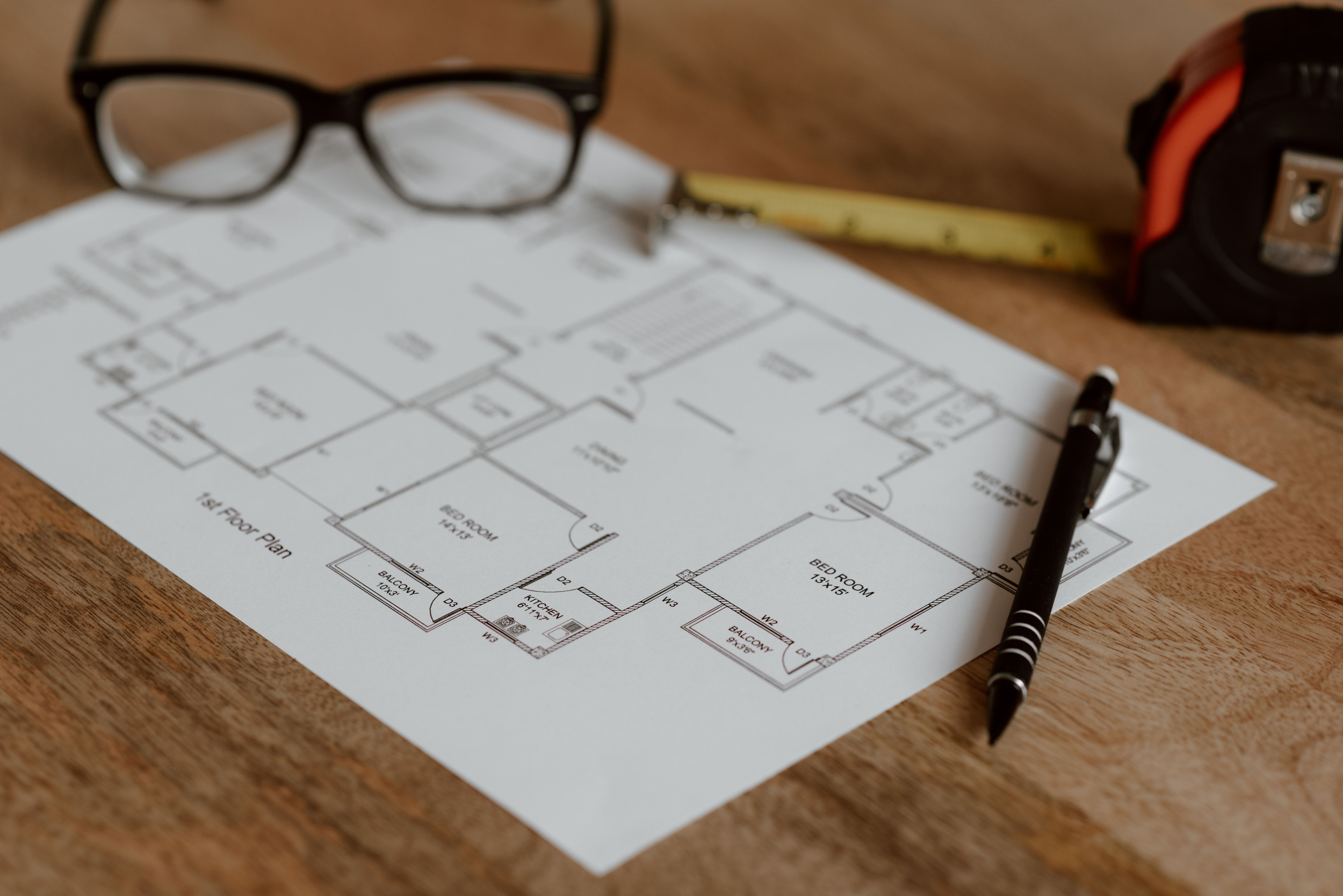 A detailed architectural floor plan resting on a wooden table alongside reading glasses, representing pre-staging layout planning in Shoreline, WA by Essential Home Staging.