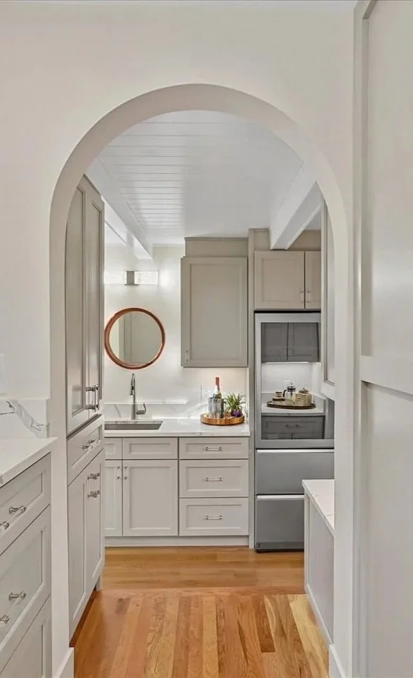 A bright and modern kitchen in a Lake Forest Park single-family home, expertly staged for real estate by Essential Home Staging, featuring white cabinets, quartz countertops, and a window looking out onto lush green trees.