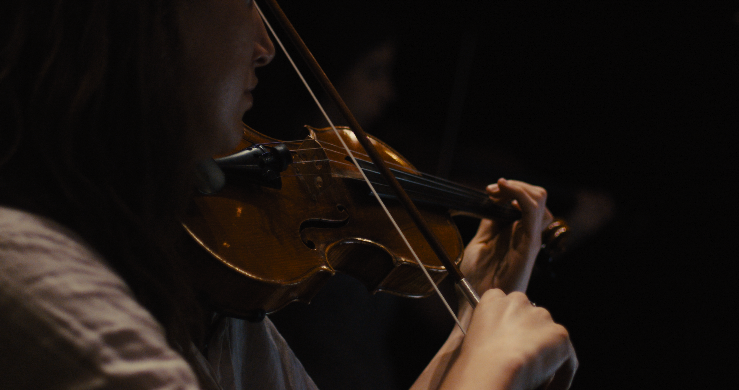 A woman playing a violin in a dark environment, focusing on her hand and the instrument.