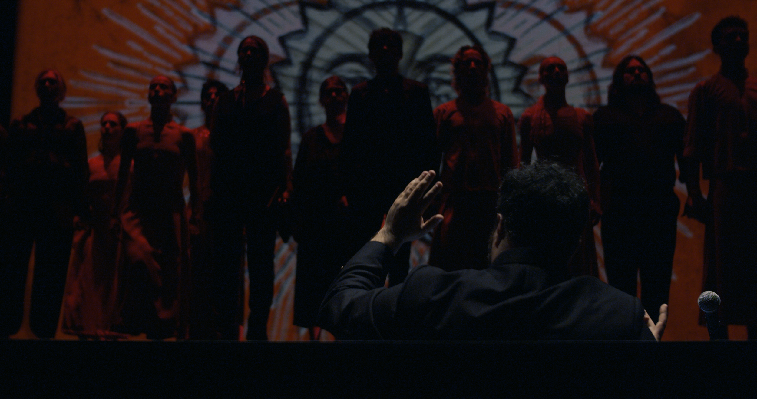 A person raising their hand towards a group of people standing in front of a large screen with abstract graphics.