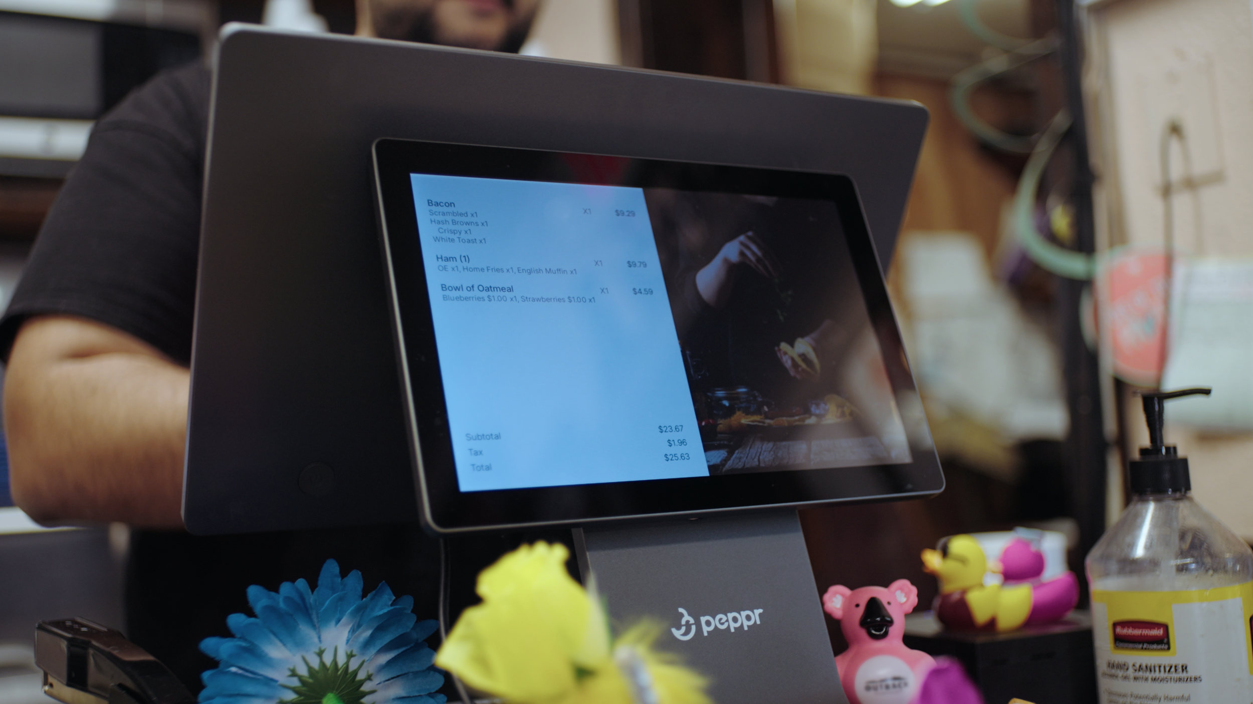 Point of sale touchscreen monitor showing order details in a restaurant, with colorful decorative items and hand sanitizer bottle in the foregroundproduction company Fort Worth. video production.
