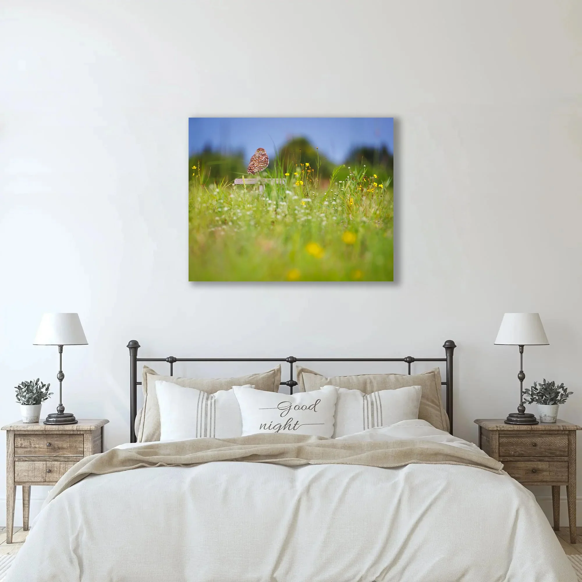 A metal print of a burrowing owl hangs above the bed of a rustic bedroom.