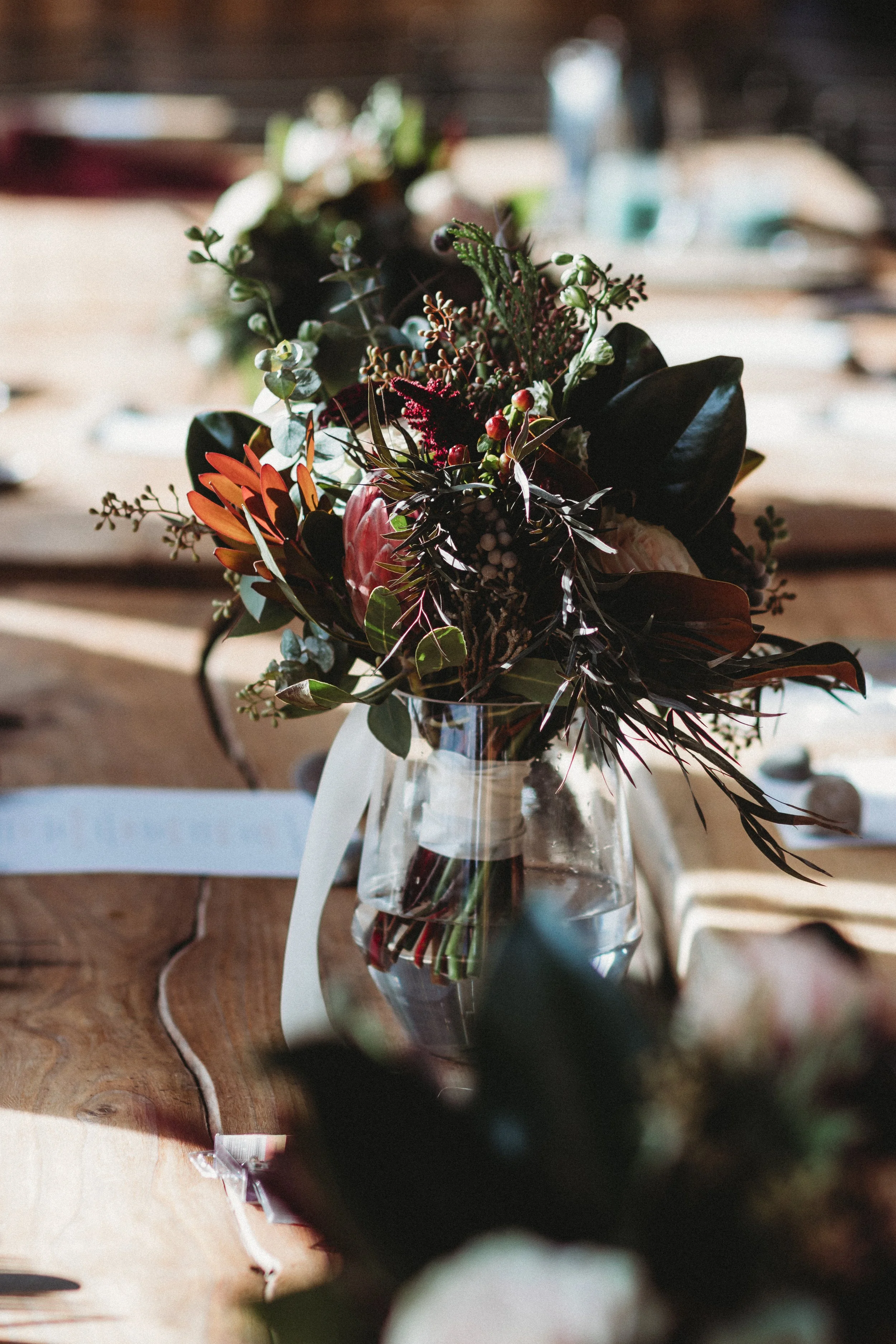 A floral arrangement in a glass vase on a wooden table, with blurred background.