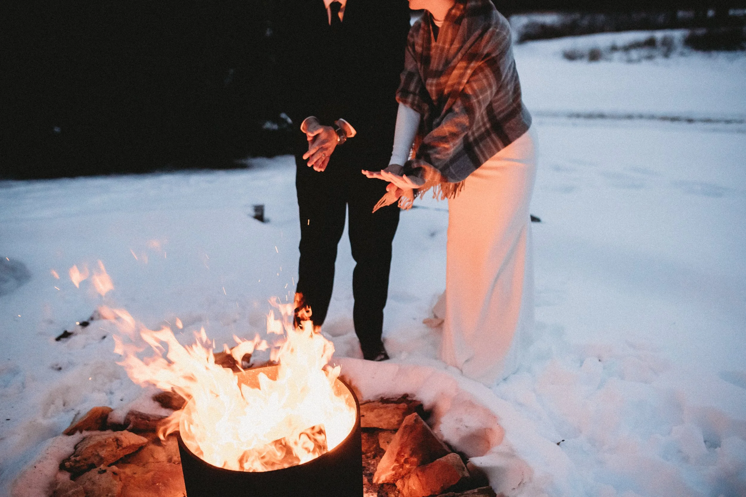 bride and groom warming by the fire pit at their snowy January wedding at the Burning Barrel in LeCompton Kansas