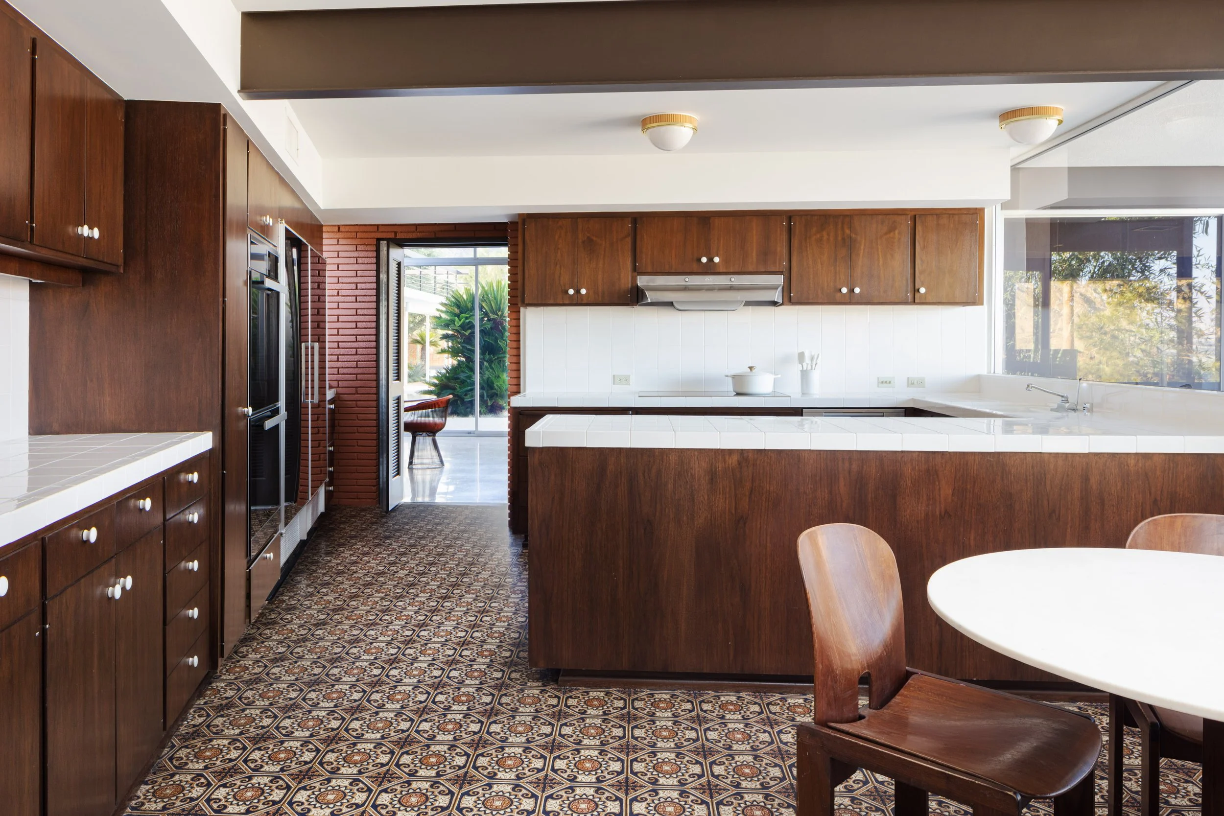 Midcentury modern kitchen with dark wood cabinets, white tile countertops, patterned floor tiles, central island, and dining table