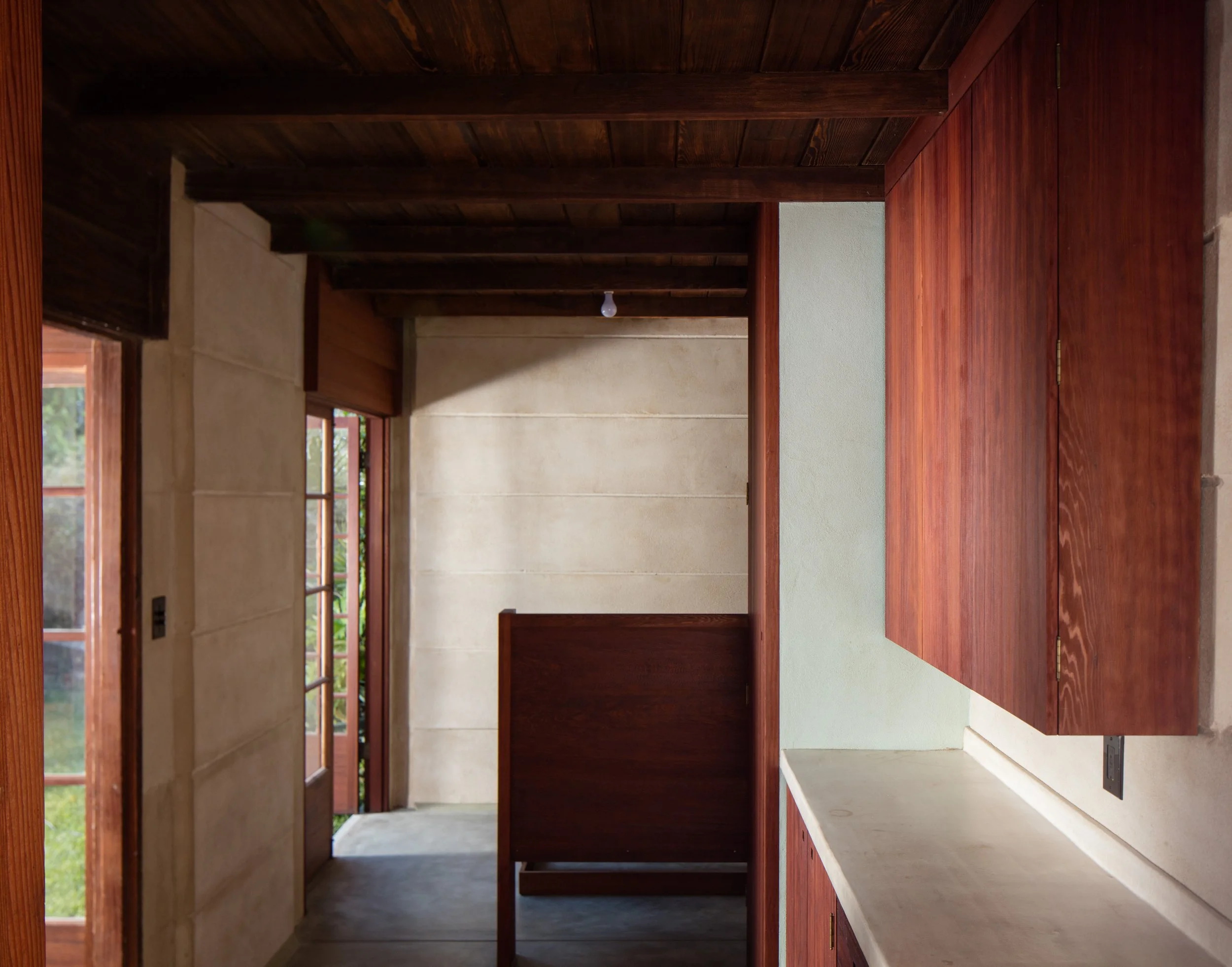 Rustic home interior with exposed wooden ceiling beams, wood cabinetry, concrete countertops, and large windows