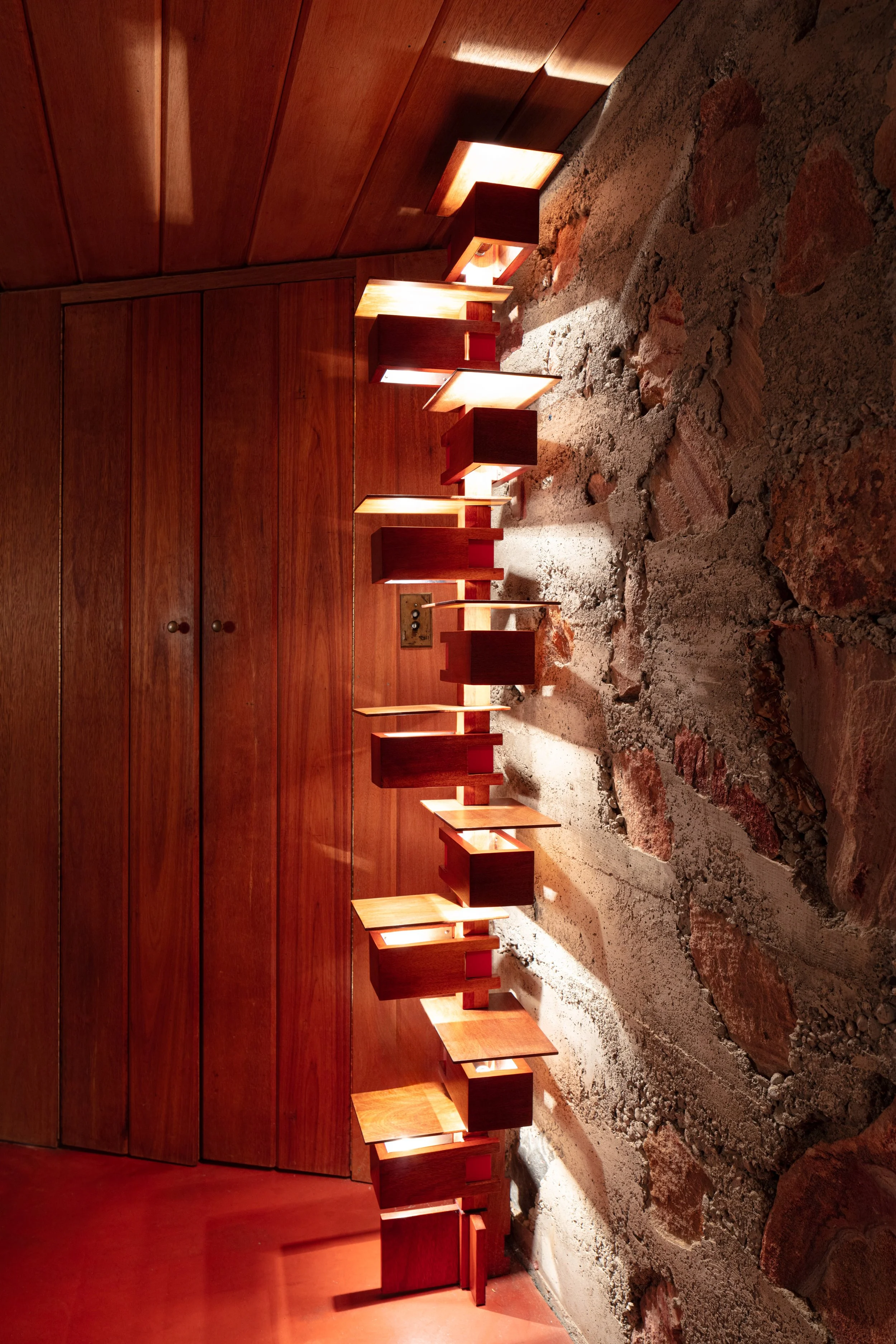 Warmly lit rustic interior with wooden ceiling, built-in shelves, storage cabinets, and exposed stone walls