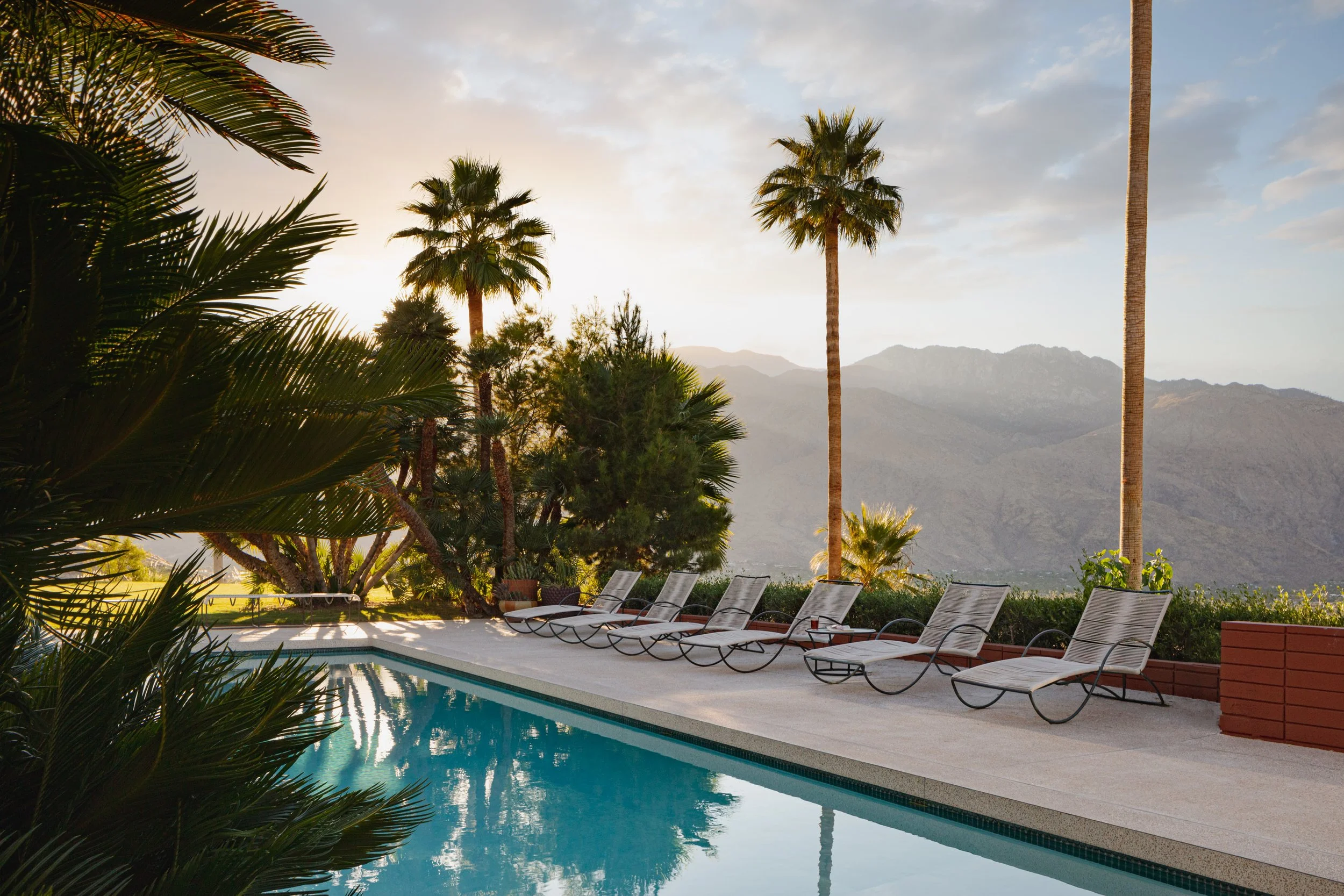 Resort pool with lounge chairs and palm trees overlooking desert mountains at sunset