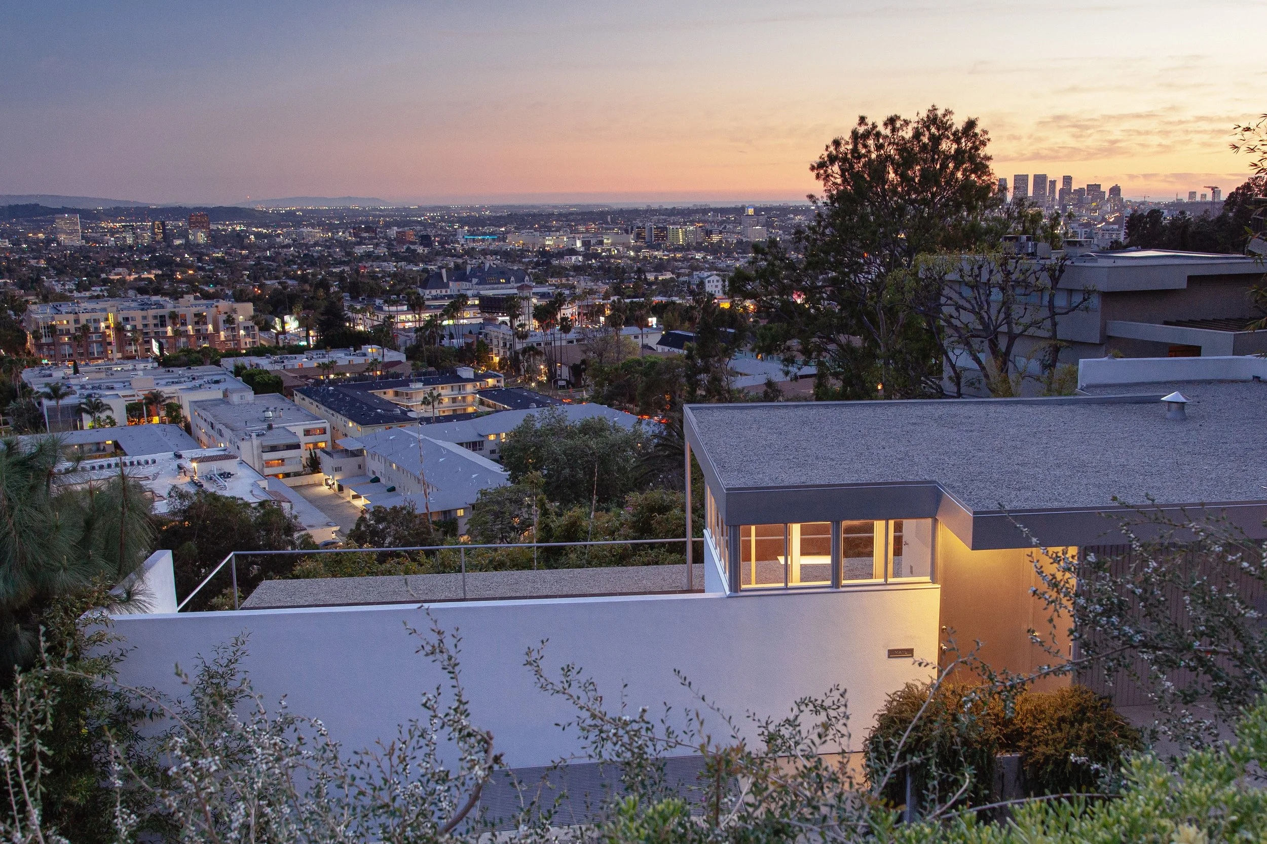 Panoramic view of Los Angeles at sunset, with downtown skyscrapers, residential neighborhoods, and modern homes in the foreground