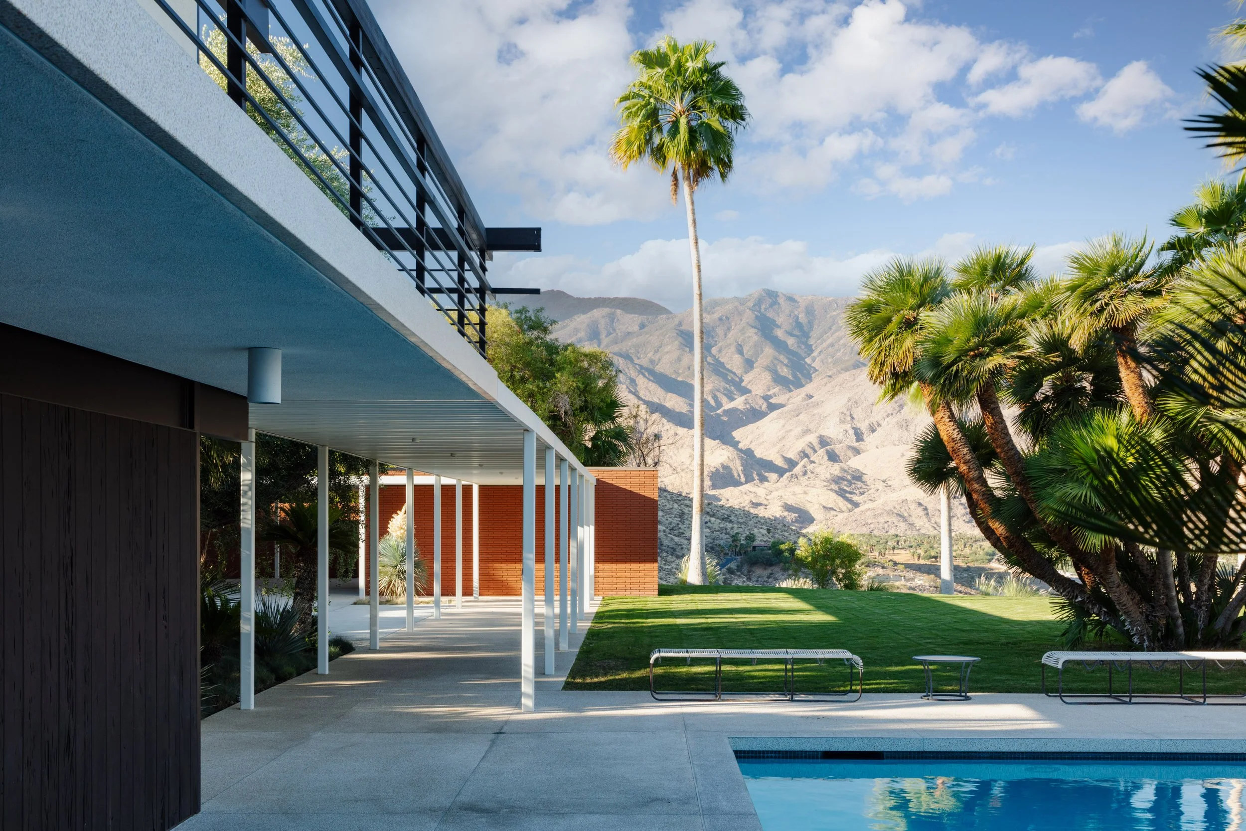 Modern midcentury home with swimming pool, palm trees, lawn, and mountain views
