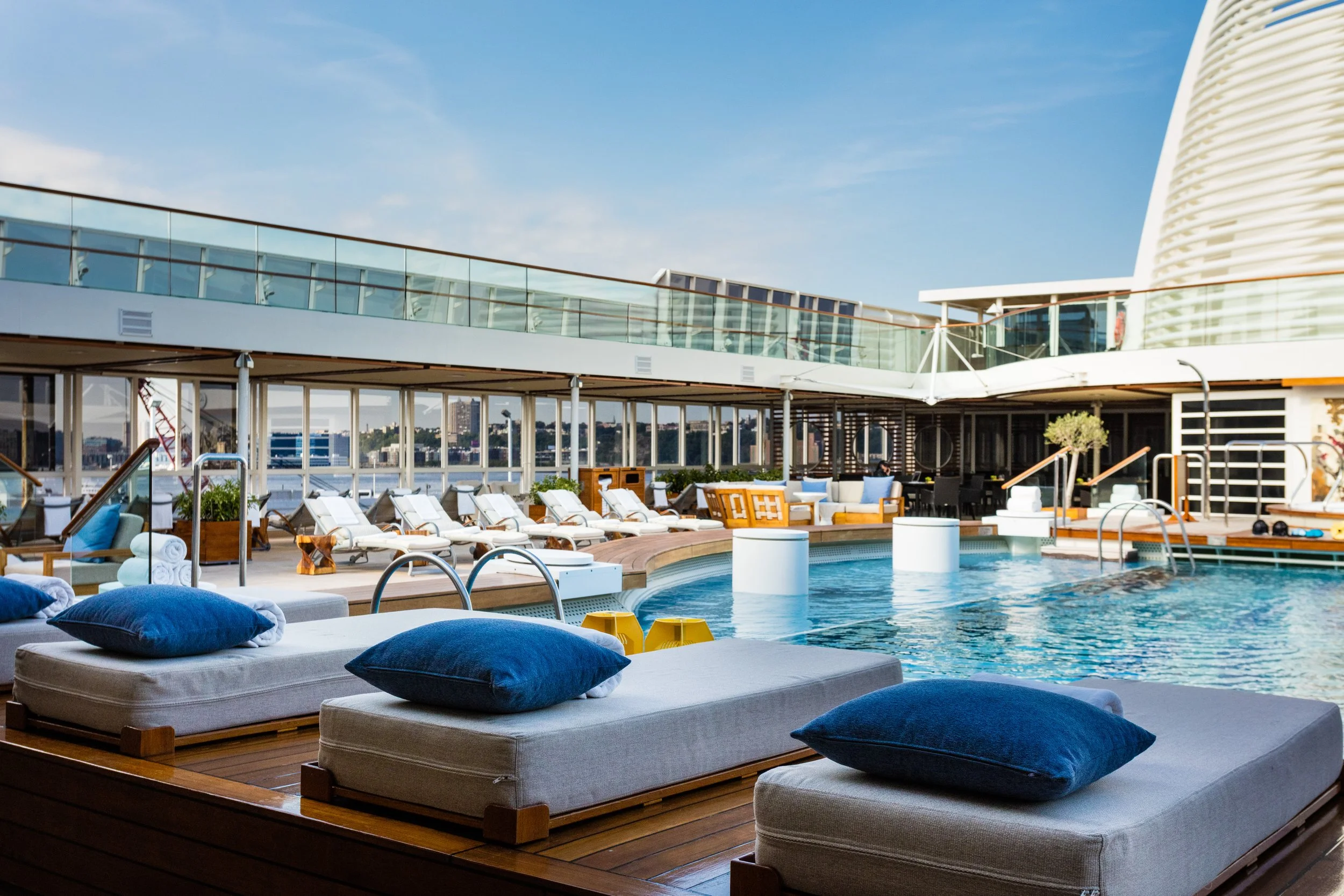 Luxury rooftop pool deck with lounge chairs, blue cushions, and waterfront city views
