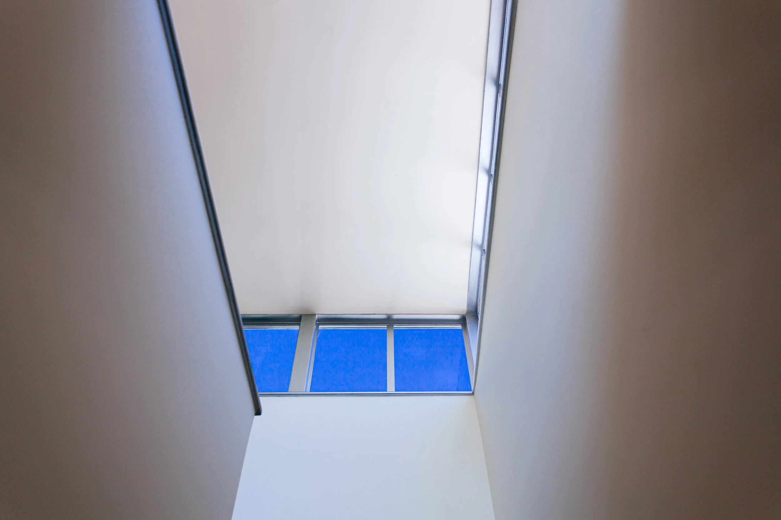 Upward view of a modern hallway with white walls, a large skylight, and blue sky visible through the windows.