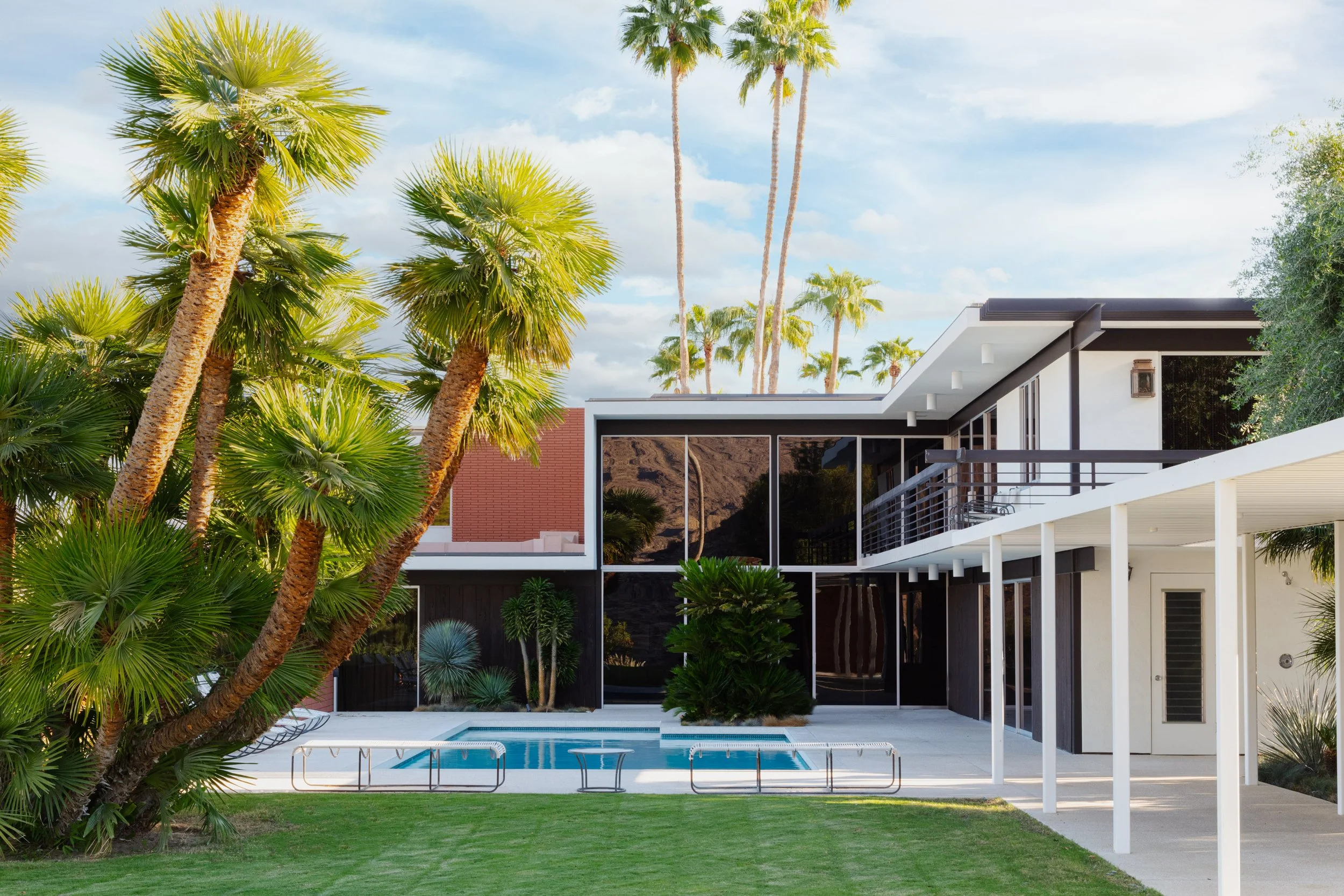 Modern midcentury home with a swimming pool, palm trees, landscaped yard, and covered patio