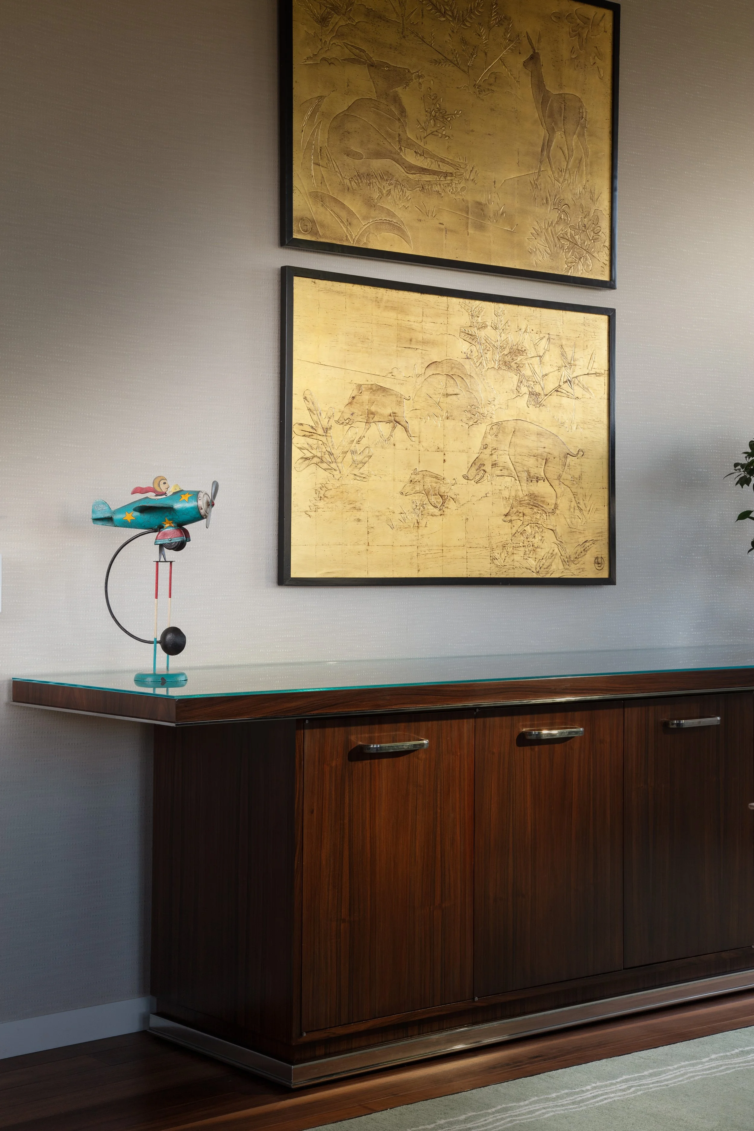 Midcentury modern sideboard with framed gold animal artwork and a vintage toy airplane sculpture
