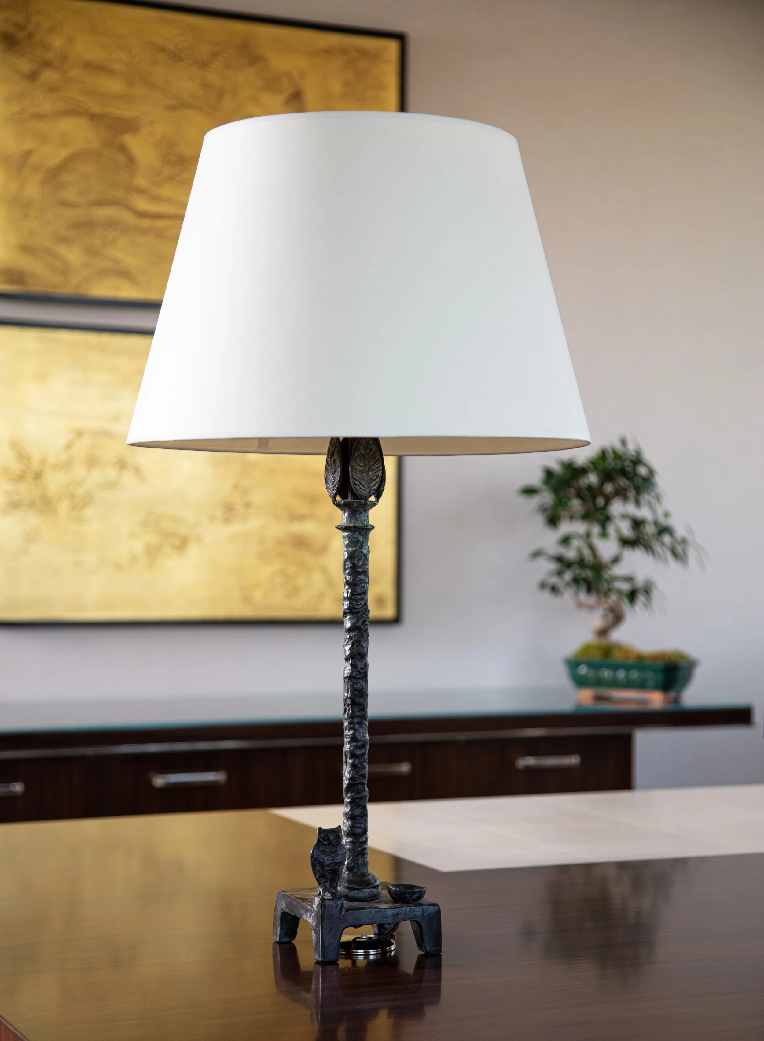 White-shaded table lamp with a sculptural dark metal base on a wooden table in a modern living room