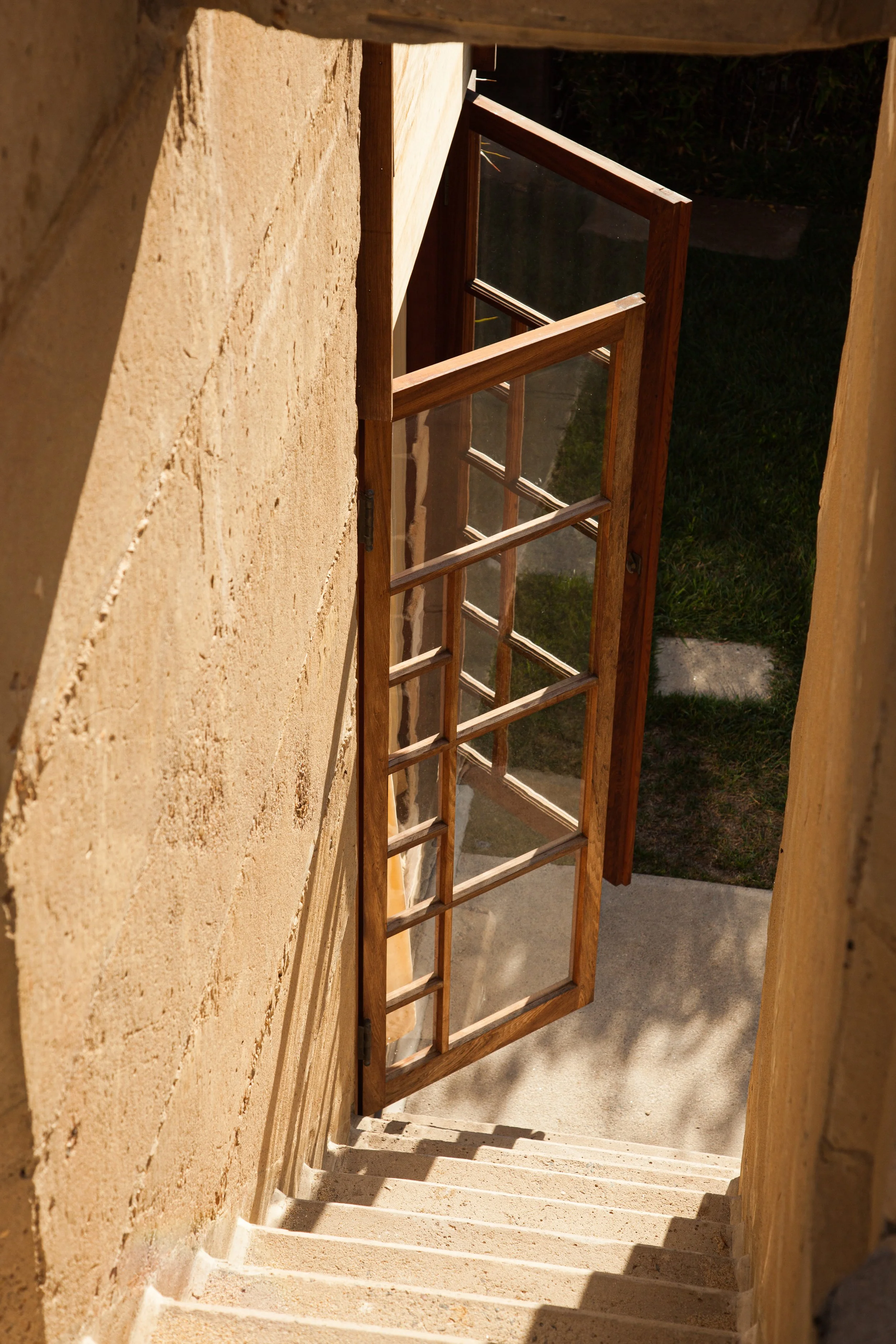 Open wooden glass door beside sunlit stone stairs