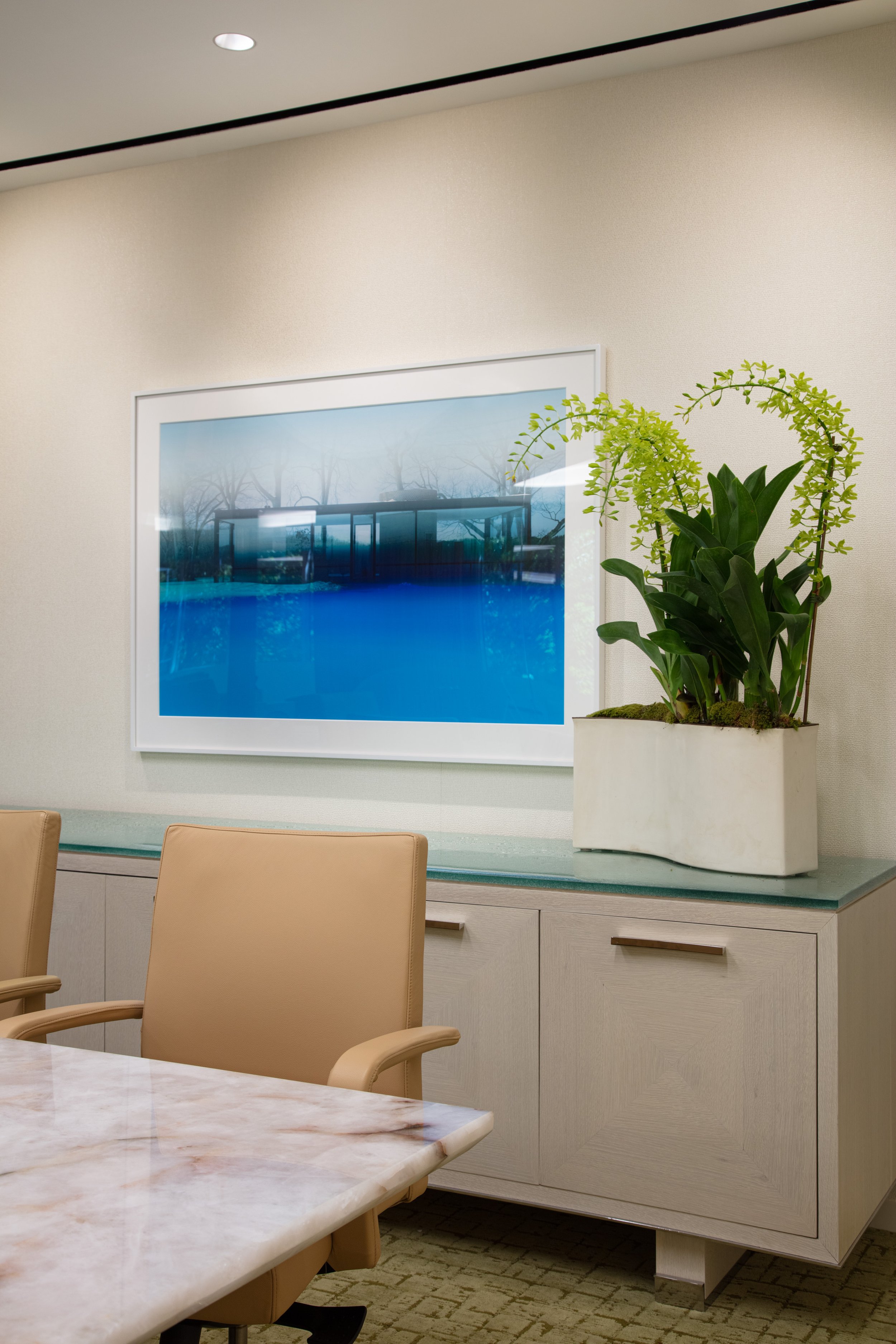 Modern office conference room with a marble table, tan chairs, framed pool photograph, and potted plant