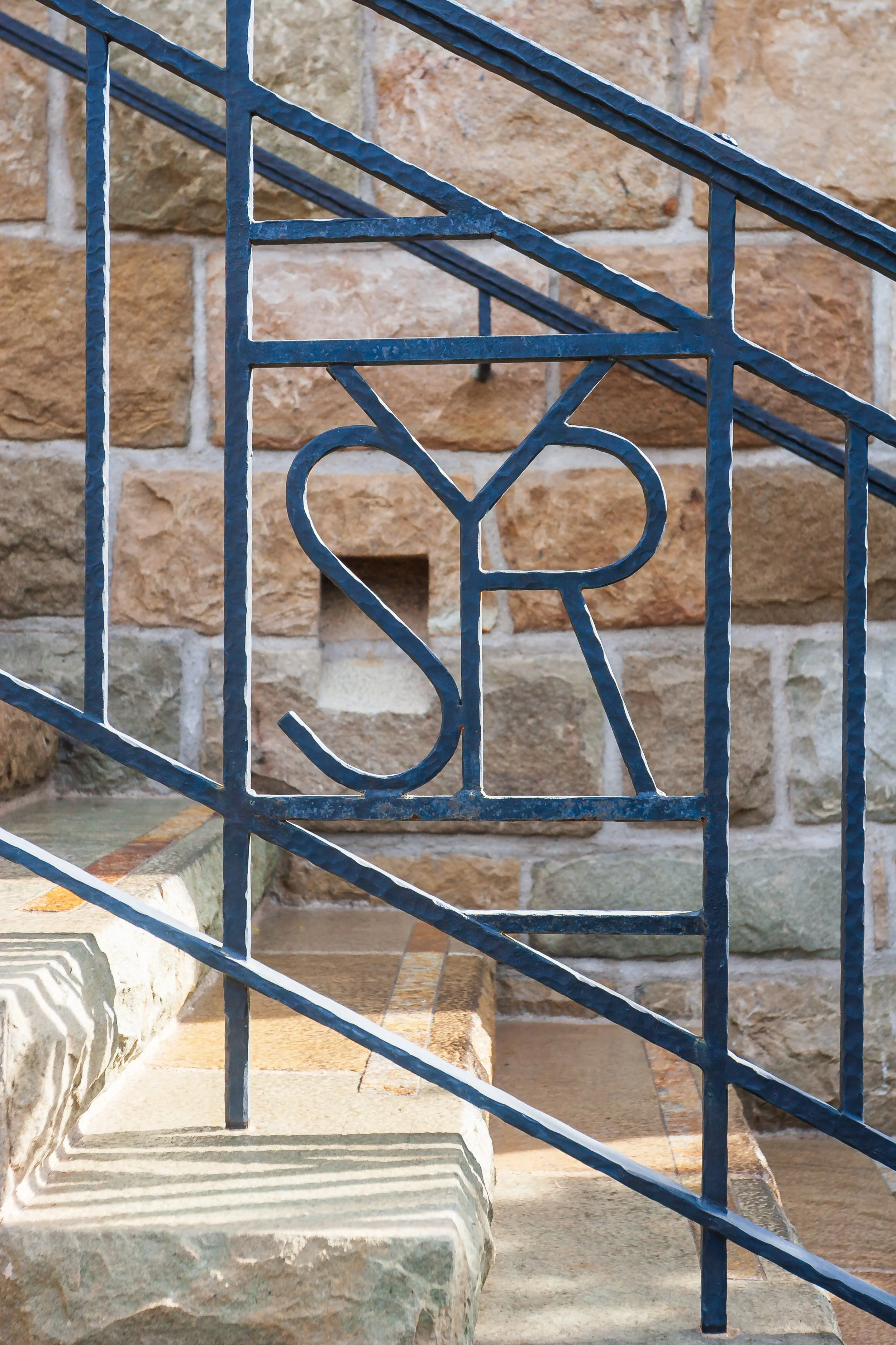 Close-up of ornate blue wrought-iron railing against a rustic stone wall
