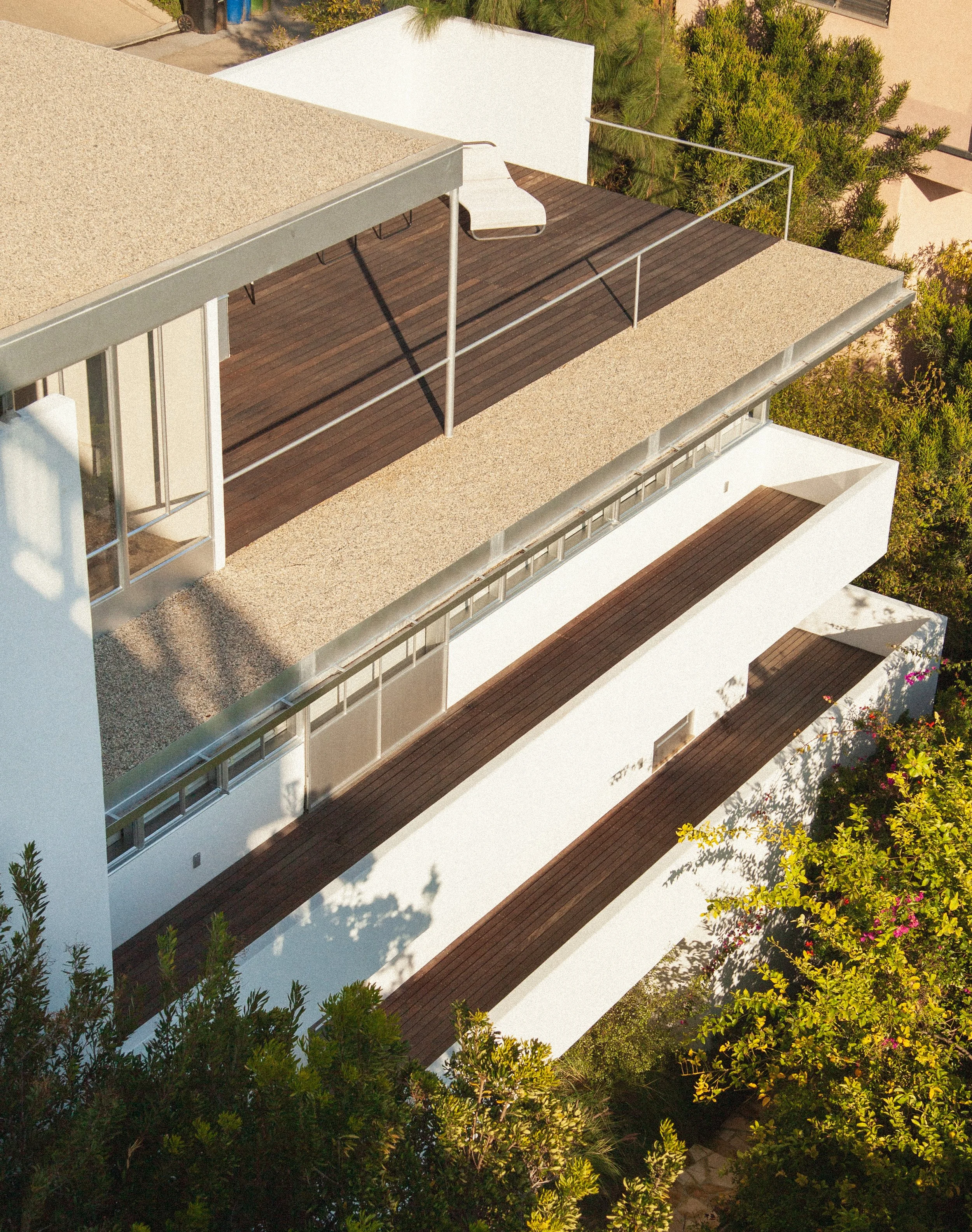 Modern white multi-level home with dark wood terraces, metal railings, and lush landscaping
