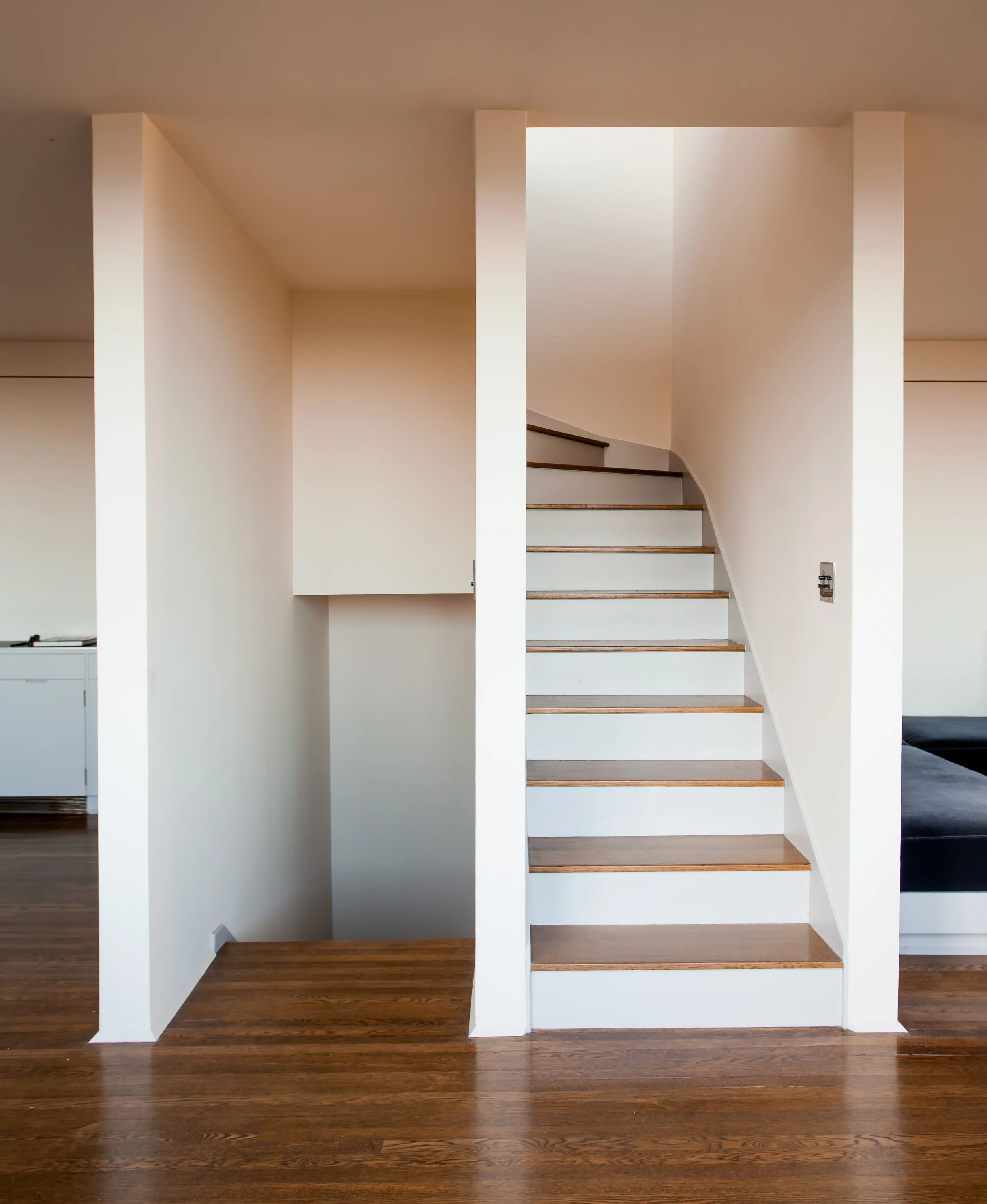 White staircase with wooden treads in a bright home interior with dark hardwood floors
