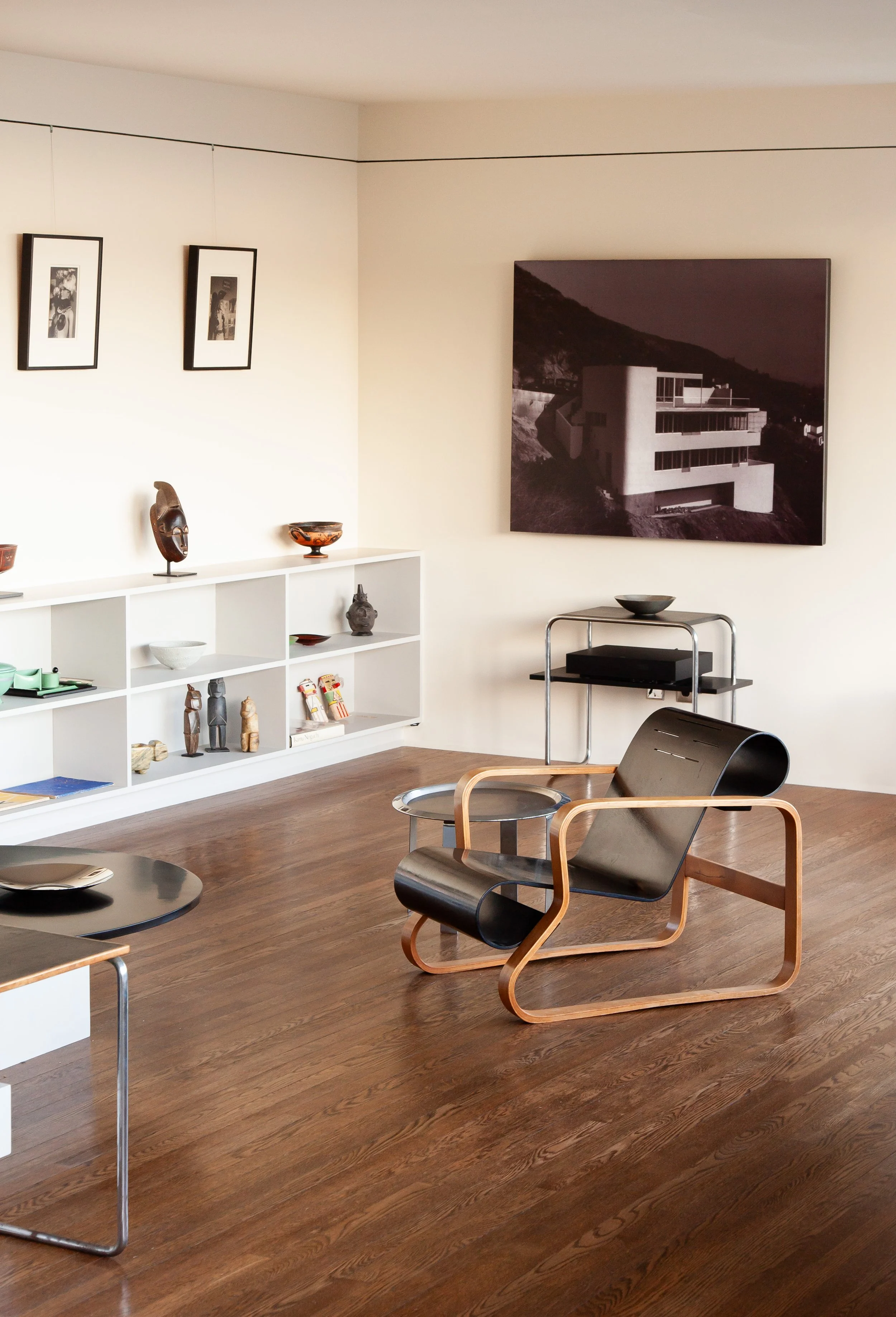 Mid-century modern living room with wood floors, sculptural furniture, built-in shelving, artwork, and a large black-and-white architectural photograph