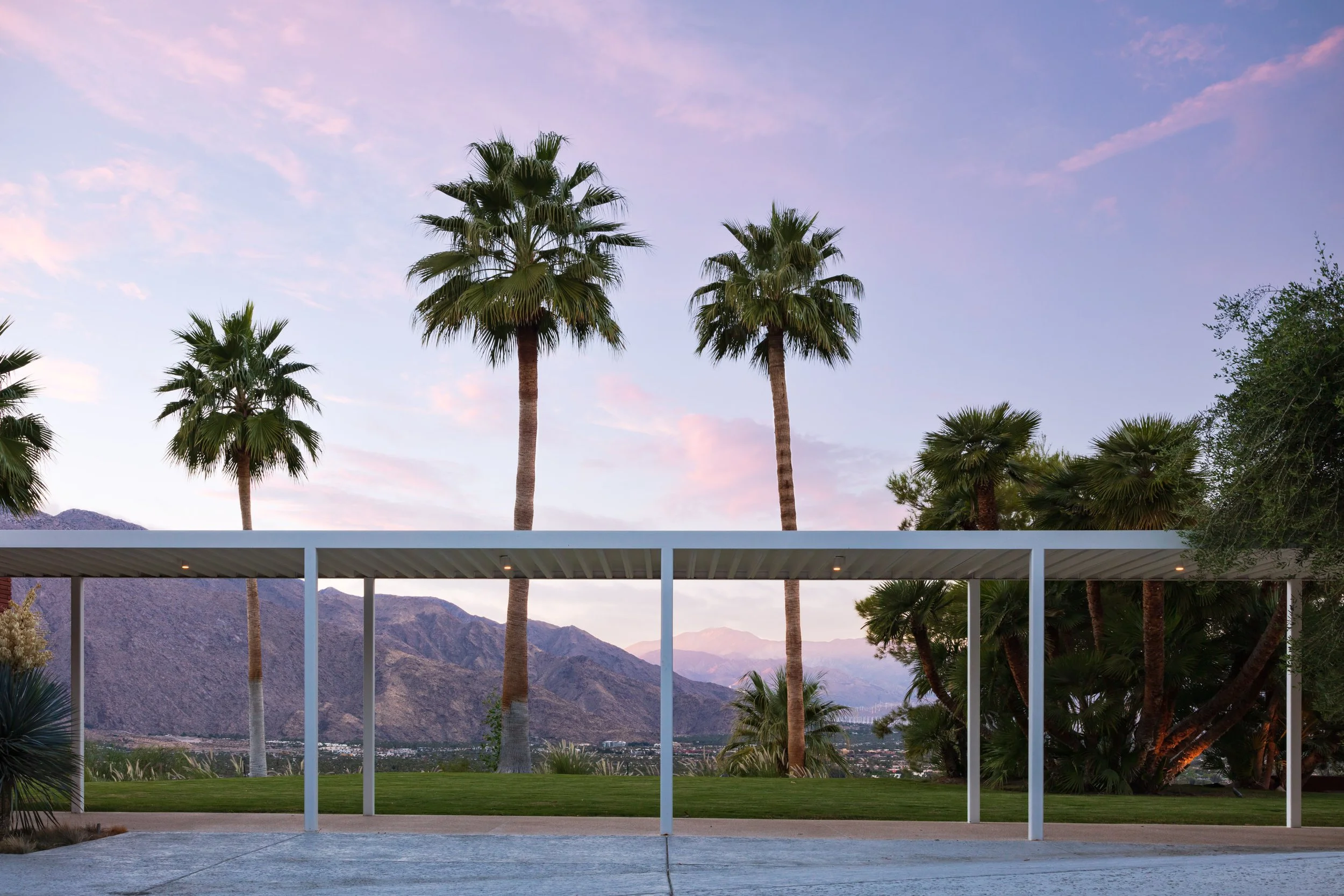 Palm trees and a modern covered patio overlooking desert mountains at sunset
