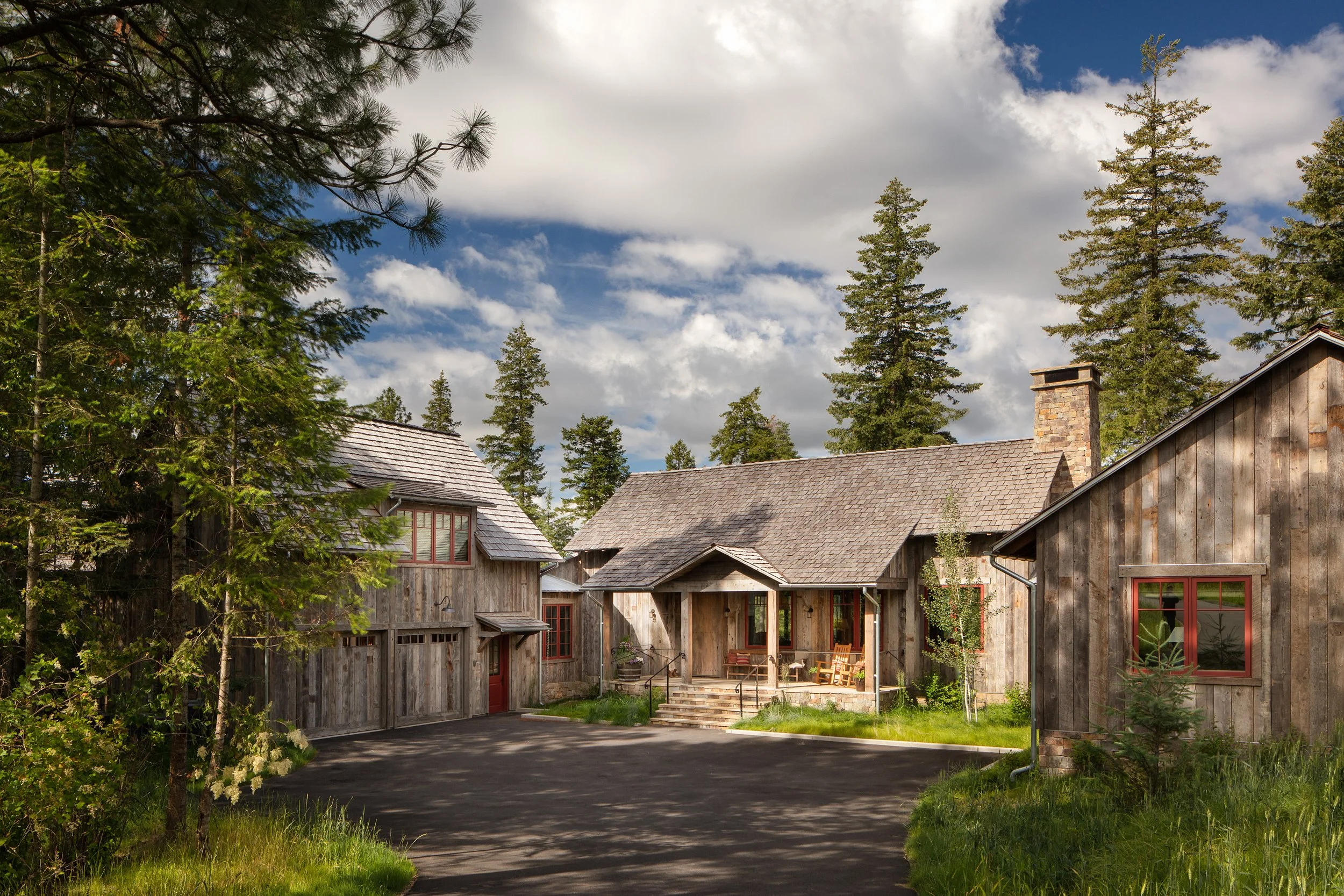 Rustic wood lodge buildings with stone chimney, surrounded by evergreen trees beneath a partly cloudy blue sky