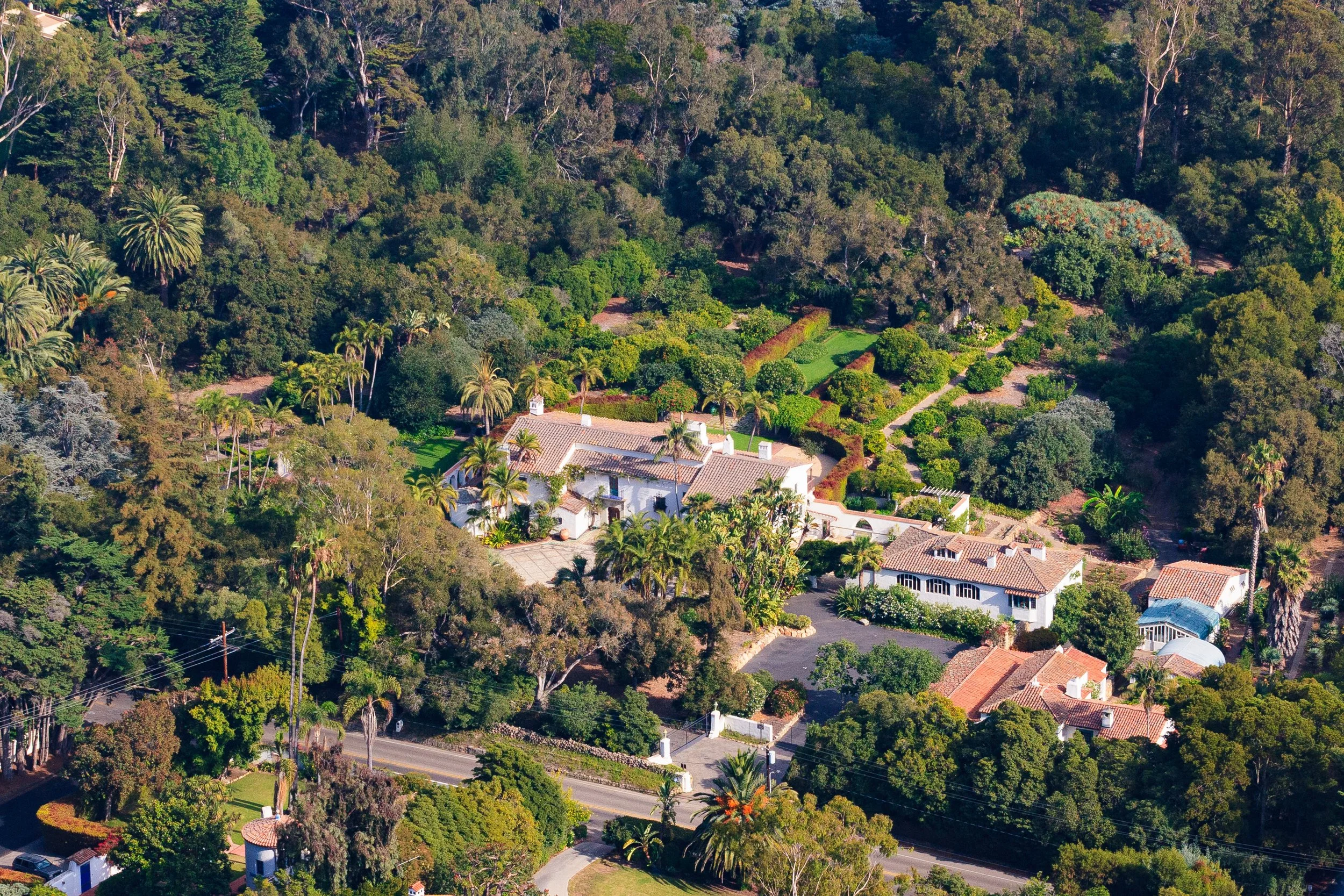 Aerial view of Spanish-style homes and landscaped gardens surrounded by lush trees and palm trees.