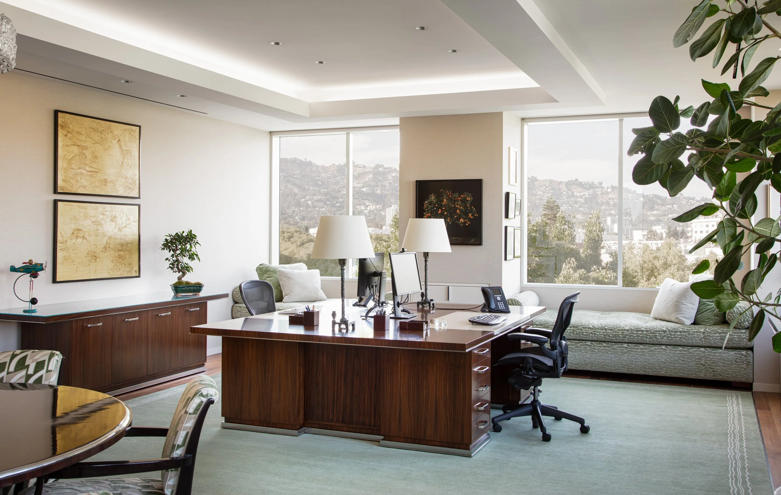 Elegant executive home office with a large wood desk, computer monitors, lamps, plants, and panoramic city views