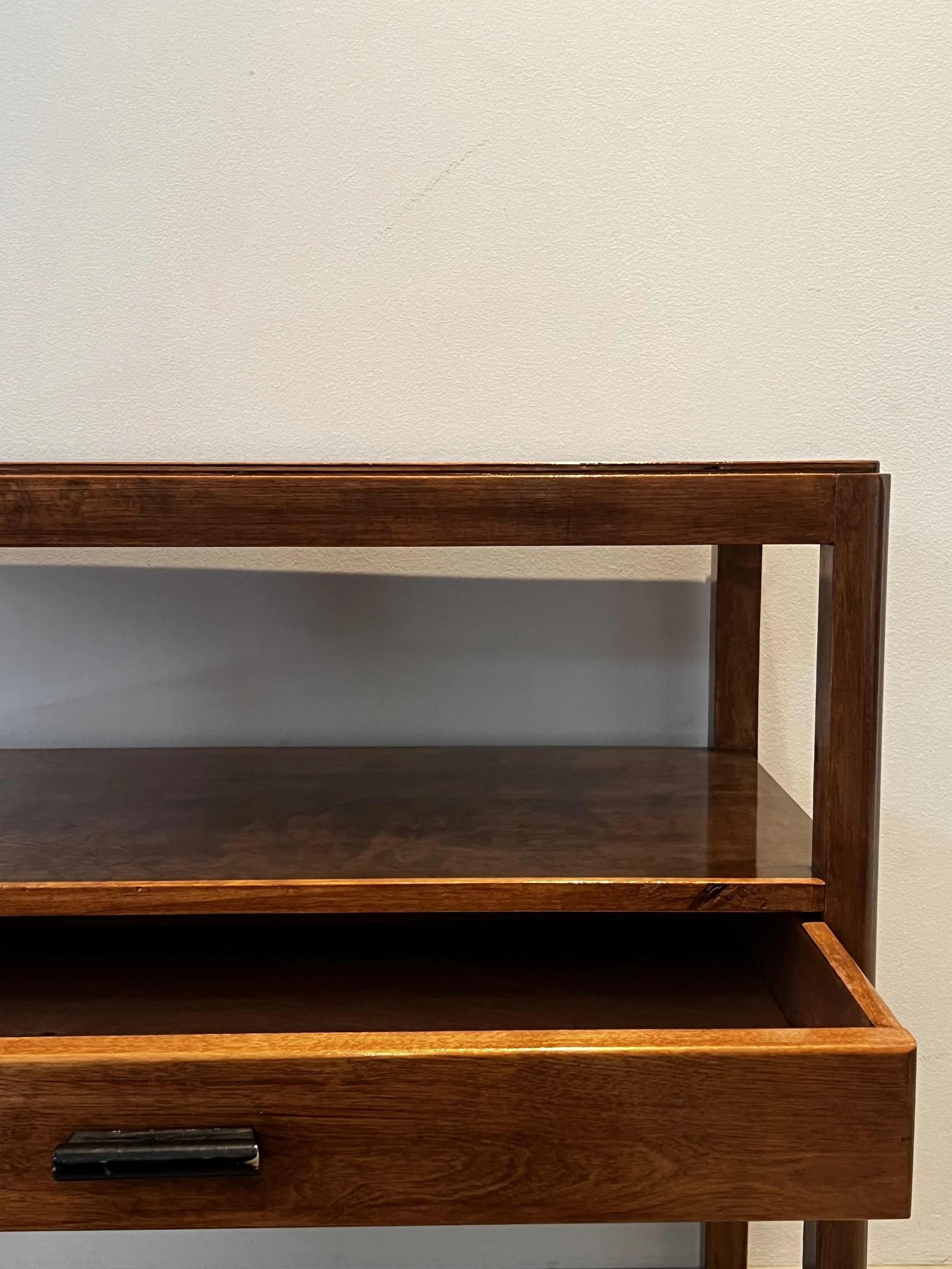 A wooden shelves unit with a drawer at the bottom, set against a plain beige wall