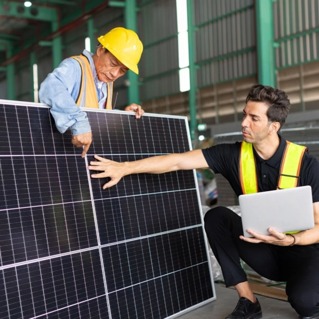 Deux hommes inspectent un panneau solaire, l'un portant un casque de sécurité jaune.