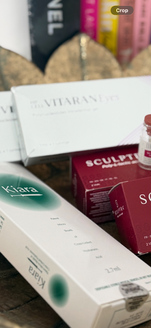 Assorted skincare and cosmetic products on a shelf, including a box labeled 'VITARAYN', a white box labeled 'Kiara', and a pink box labeled 'Sculpt' with a small jar.