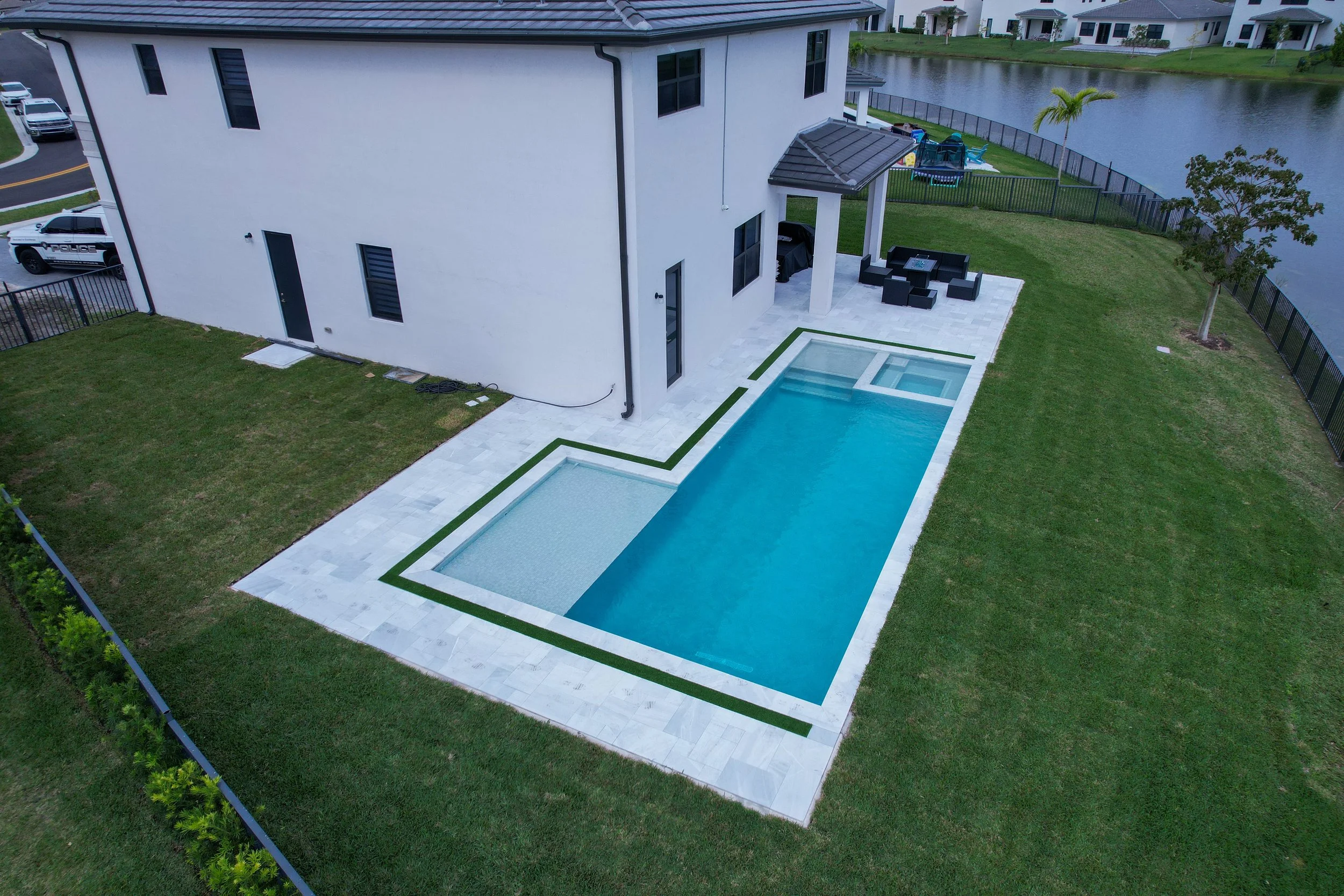 Backyard with modern rectangular swimming pool, adjacent patio furniture, and a view of a lake.