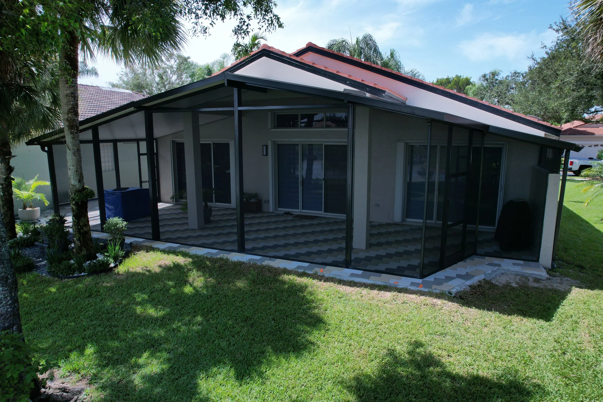 Backyard view of a modern house with a screened-in patio area and green lawn, surrounded by trees and plants.