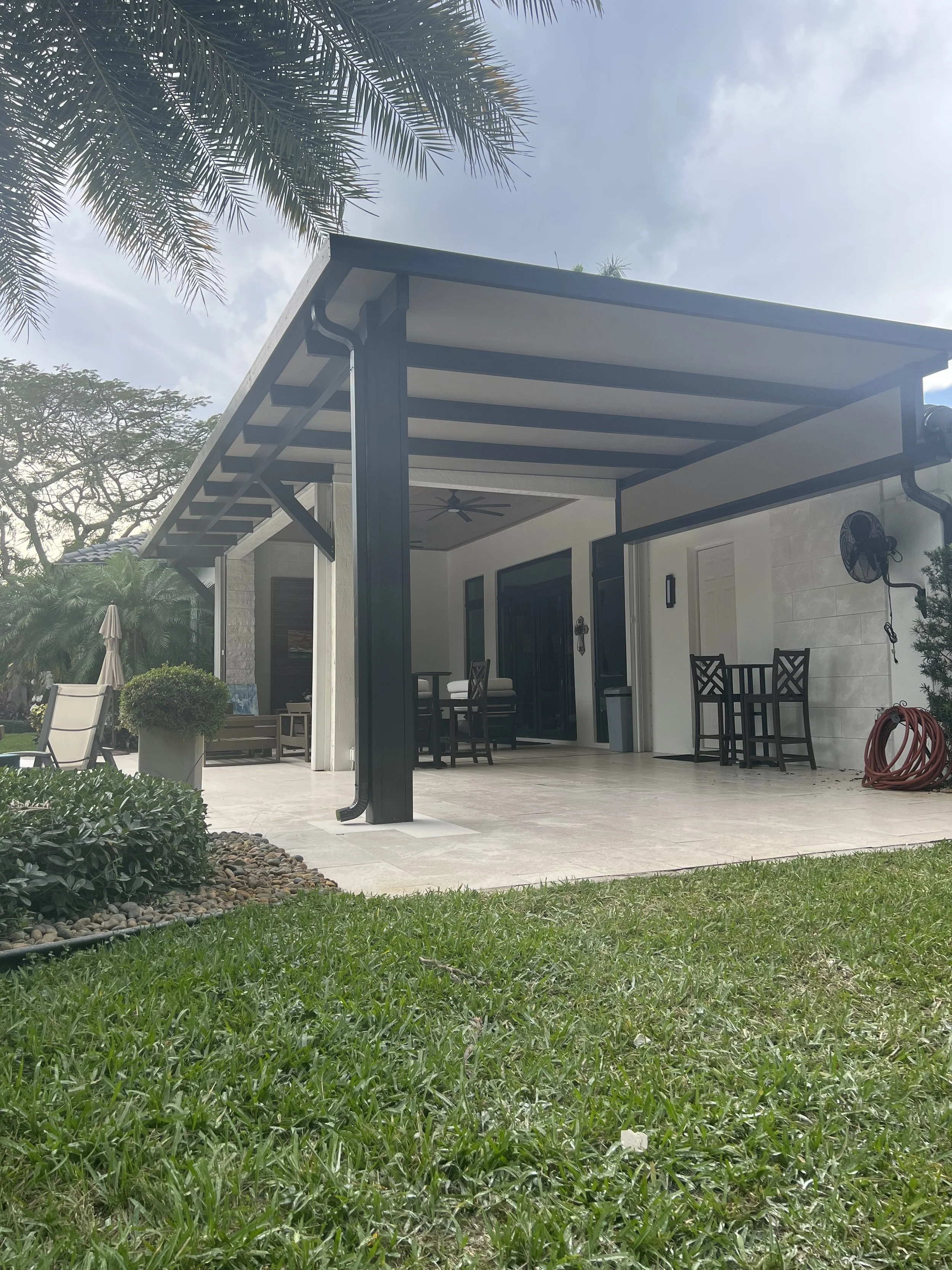 Outdoor patio with modern metal pergola, outdoor seating, and green lawn in a residential backyard.