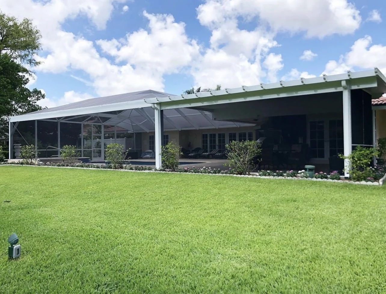 Backyard with screened patio and lawn under a blue sky with clouds.