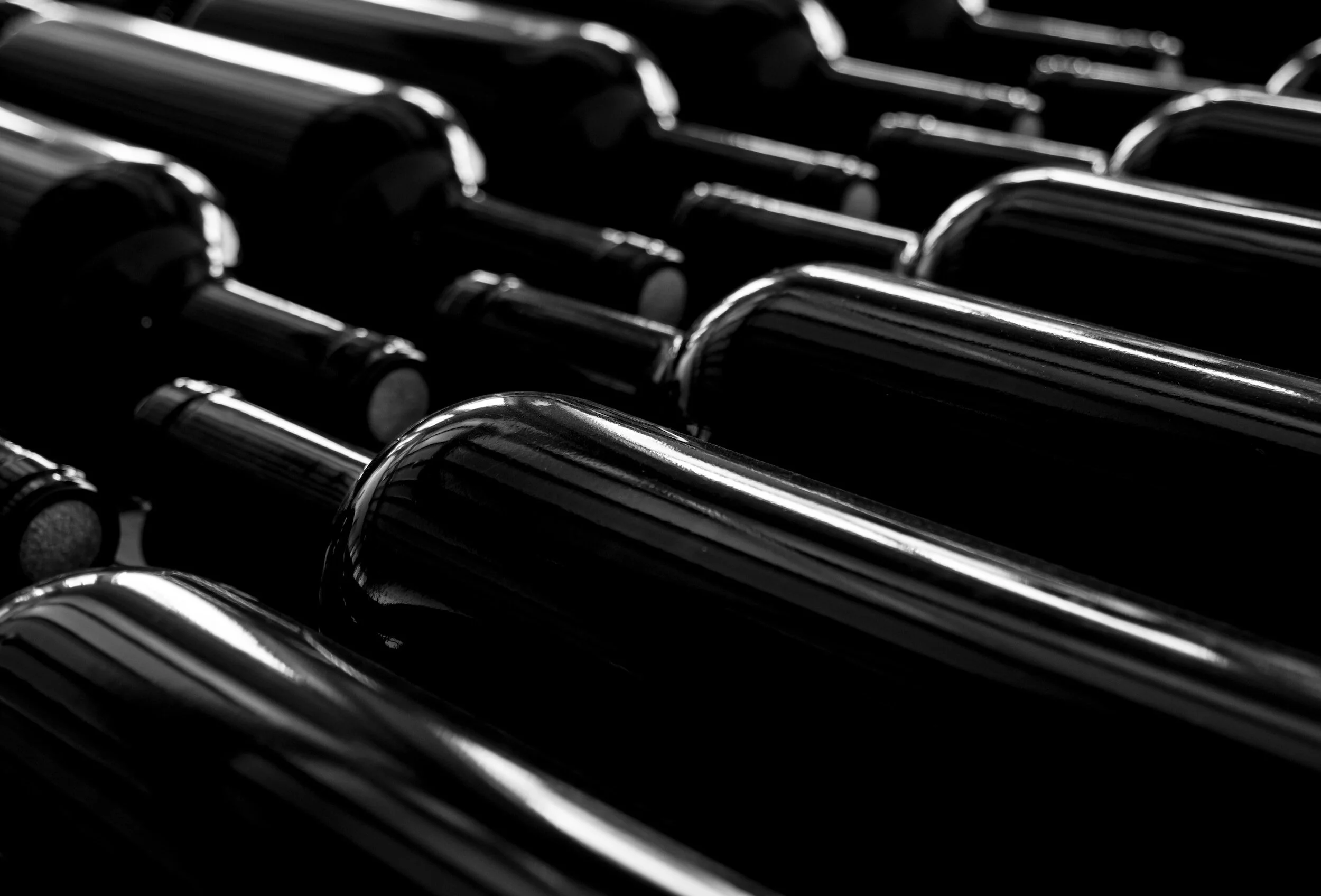 Close-up of several wine bottles stacked horizontally in black and white.