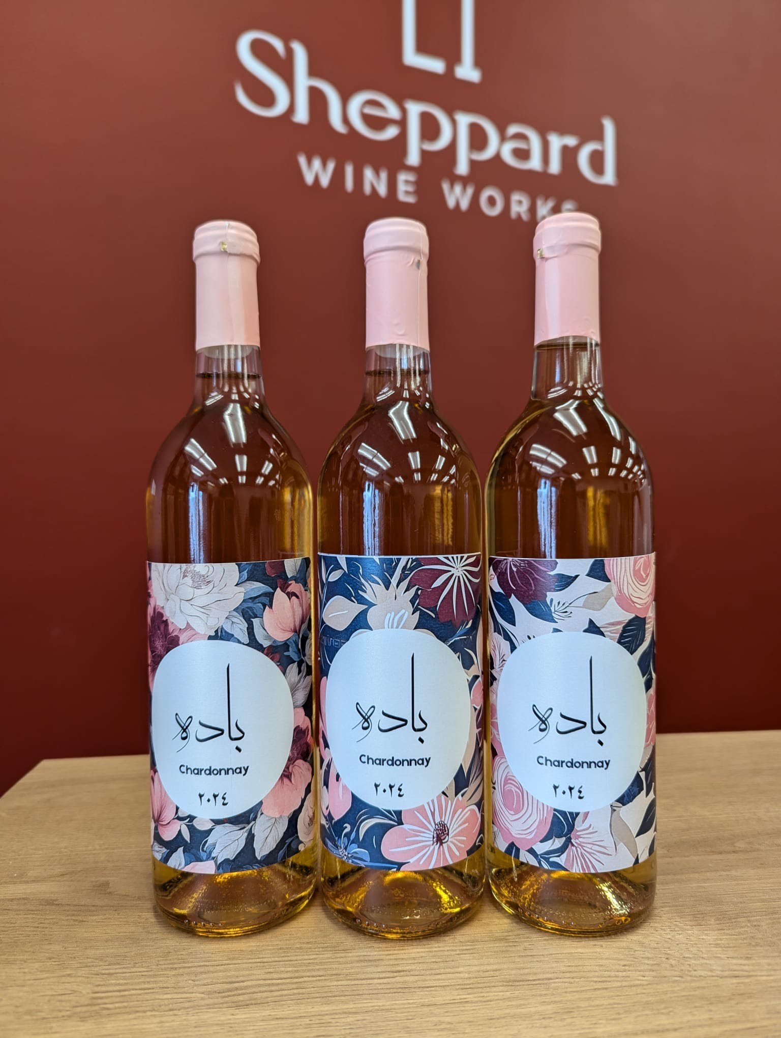 Three bottles of Chardonnay with floral labels displayed against a red background that reads 'Sheppard Wine Works.'"