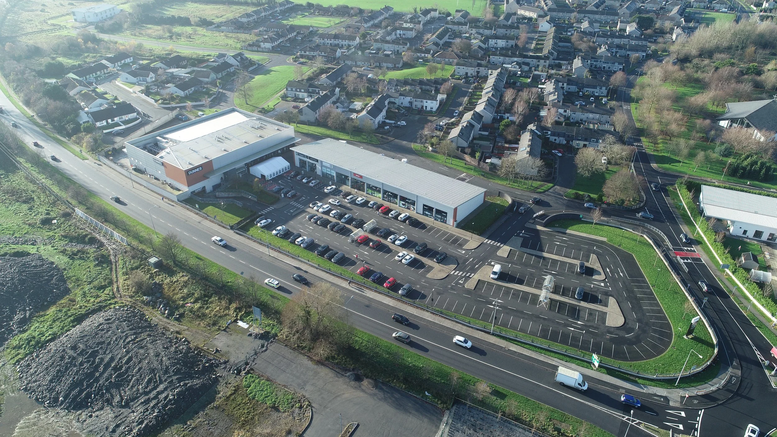 Aerial view of a shopping center with parking lot, surrounded by residential houses and roads.