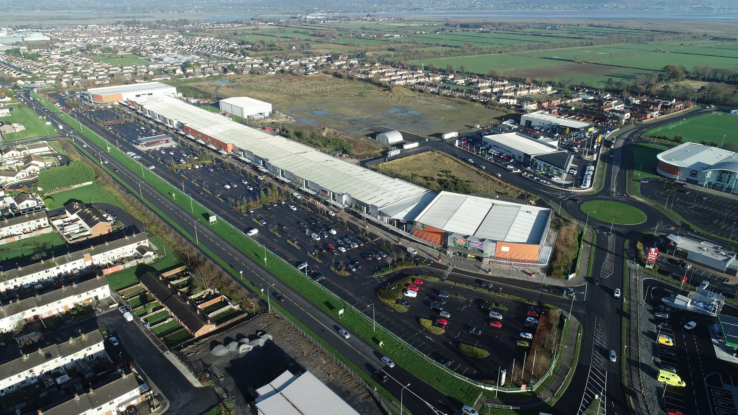 Aerial view of a shopping mall with surrounding roads, parking lots, residential neighborhoods, and green fields.