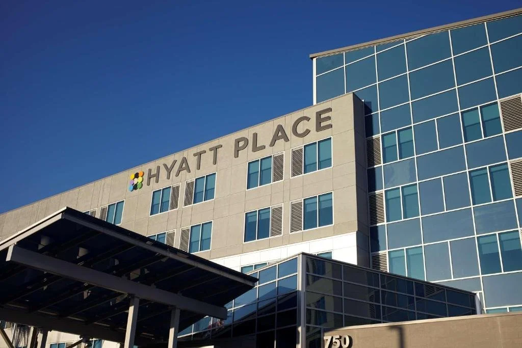 Exterior view of a modern hotel building with a sign that reads 'Hyatt Place,' with blue glass windows and a clear sky.