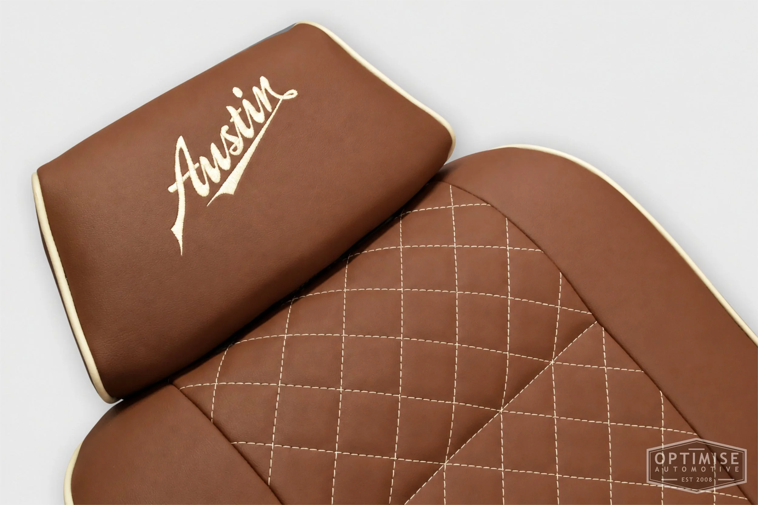 Classic Mini seat retrims featuring original single-post headrest front seats and a matching MK4 rear seat, trimmed in dark tan leatherette with cream diamond stitching and piping, with embroidered headrests.