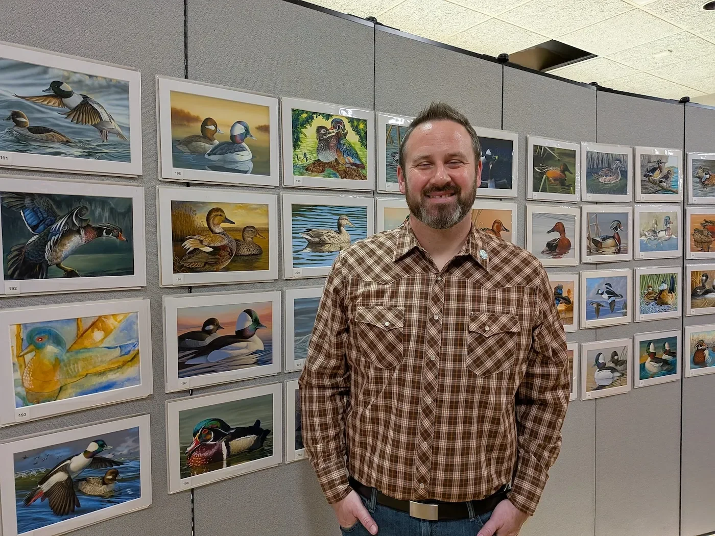 A man standing smiling in front of a wall of duck paintings
