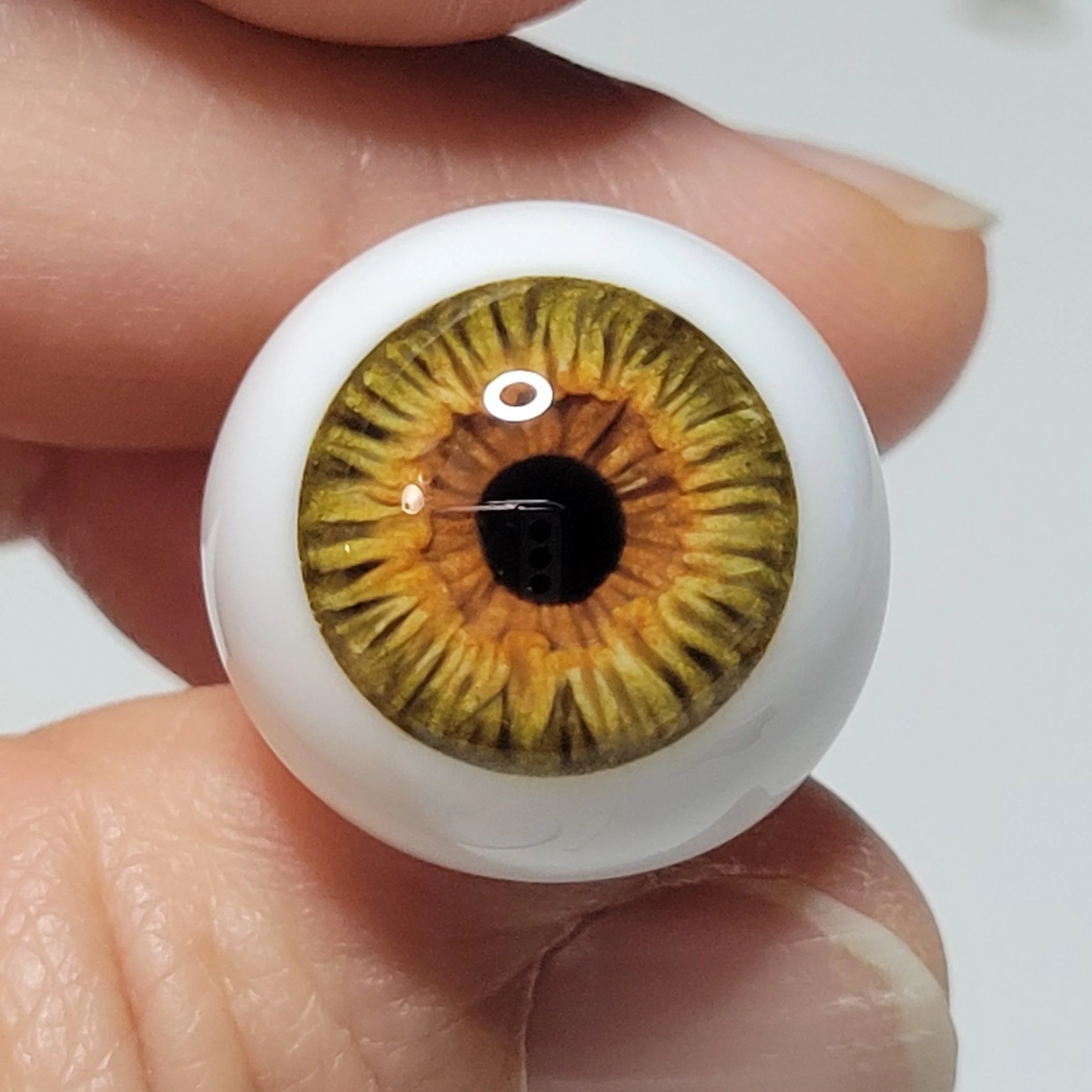 Close-up of a human eye with a light brown iris, reflected in a mirror-like surface, surrounded by skin and eyelid.