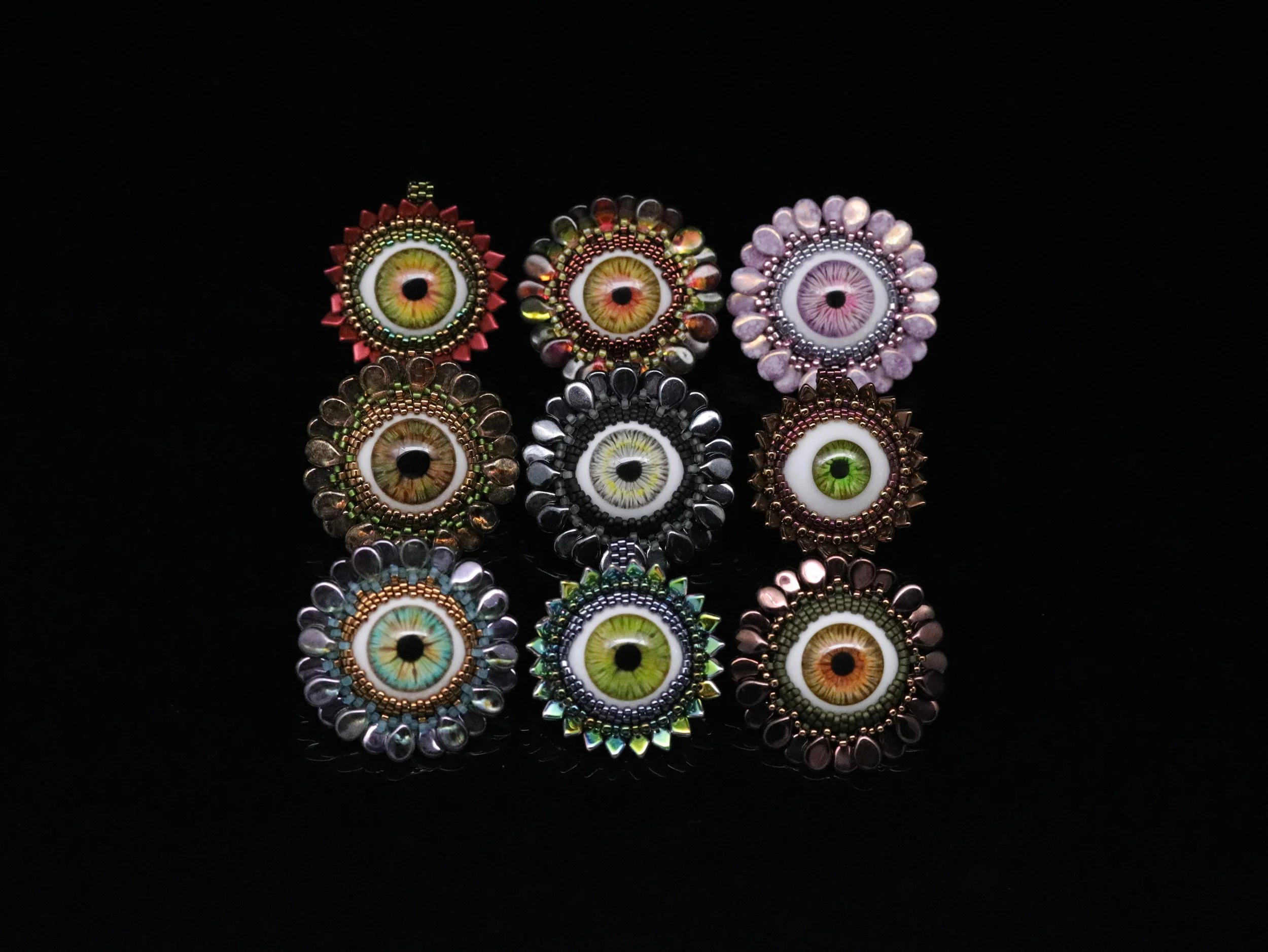 A collection of artificial eye jewelry pieces decorated with colorful beads and crystals on a black background.