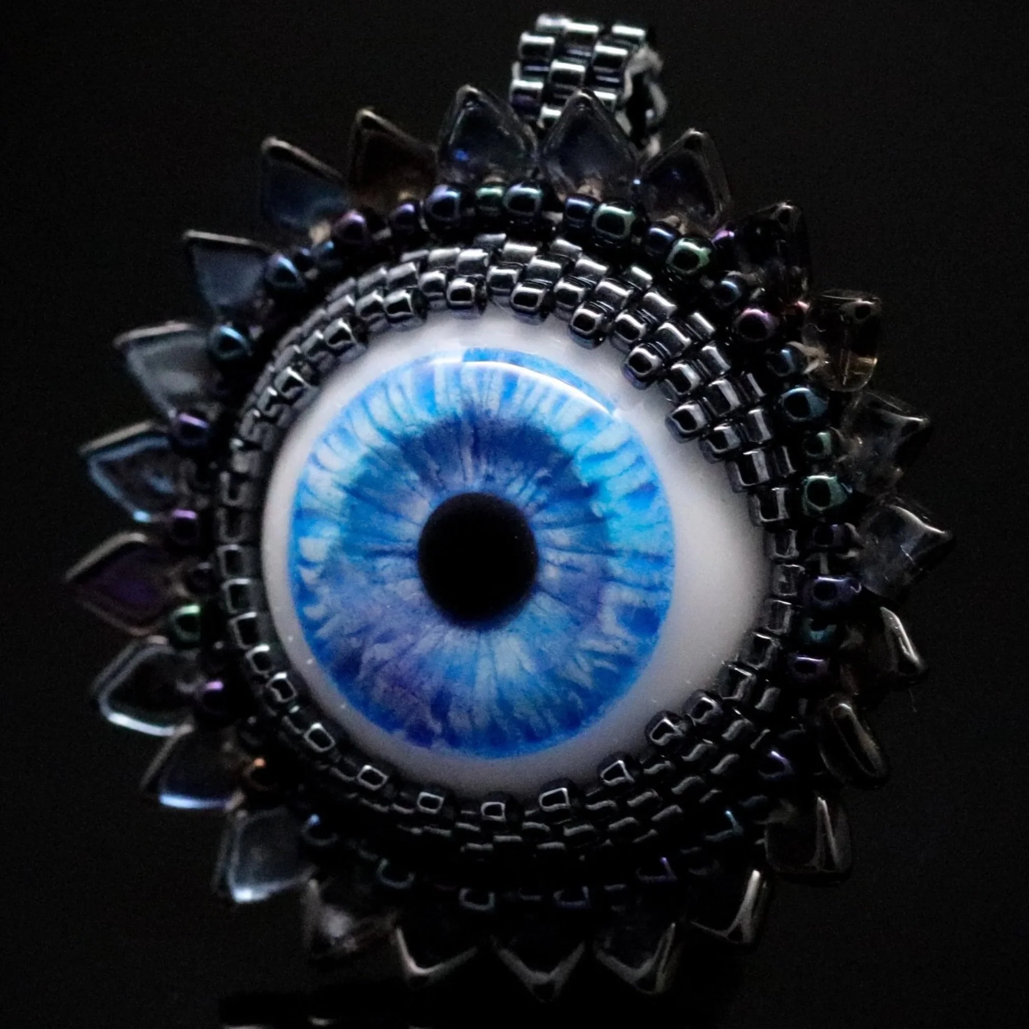Close-up of a spiral hammered bracelet with beads, featuring shades of black, silver, and iridescent colors, against a dark background.
