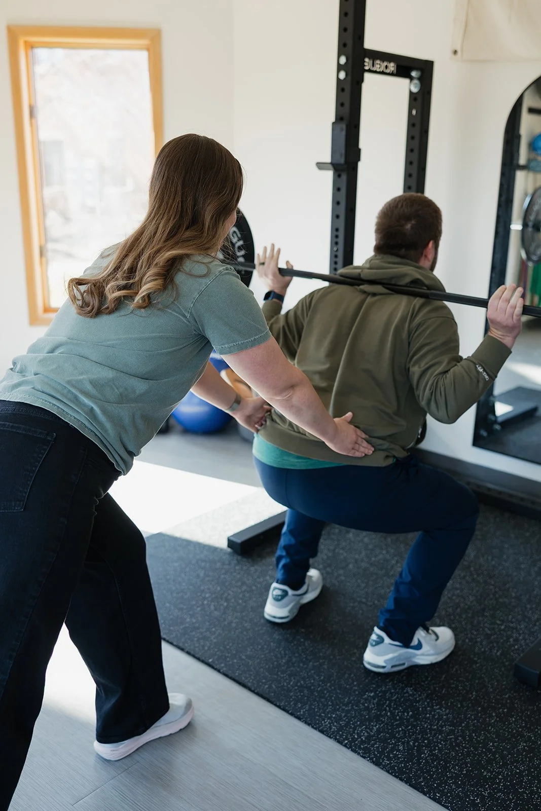 Active adult male squatting with physical therapist in clinic in Columbia, MO